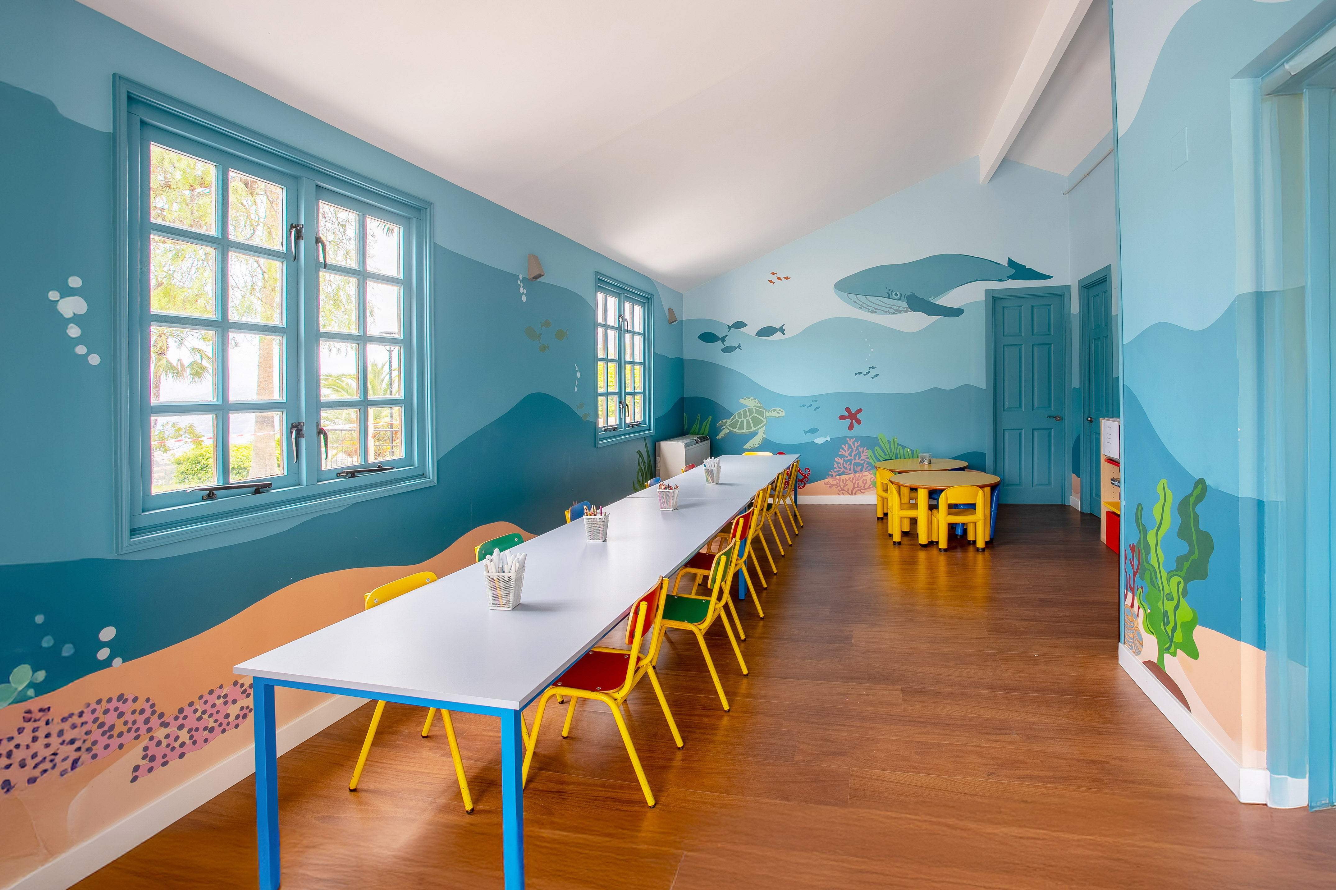 Vibrant kids' club room featuring ocean murals, activity tables, and colorful seating.