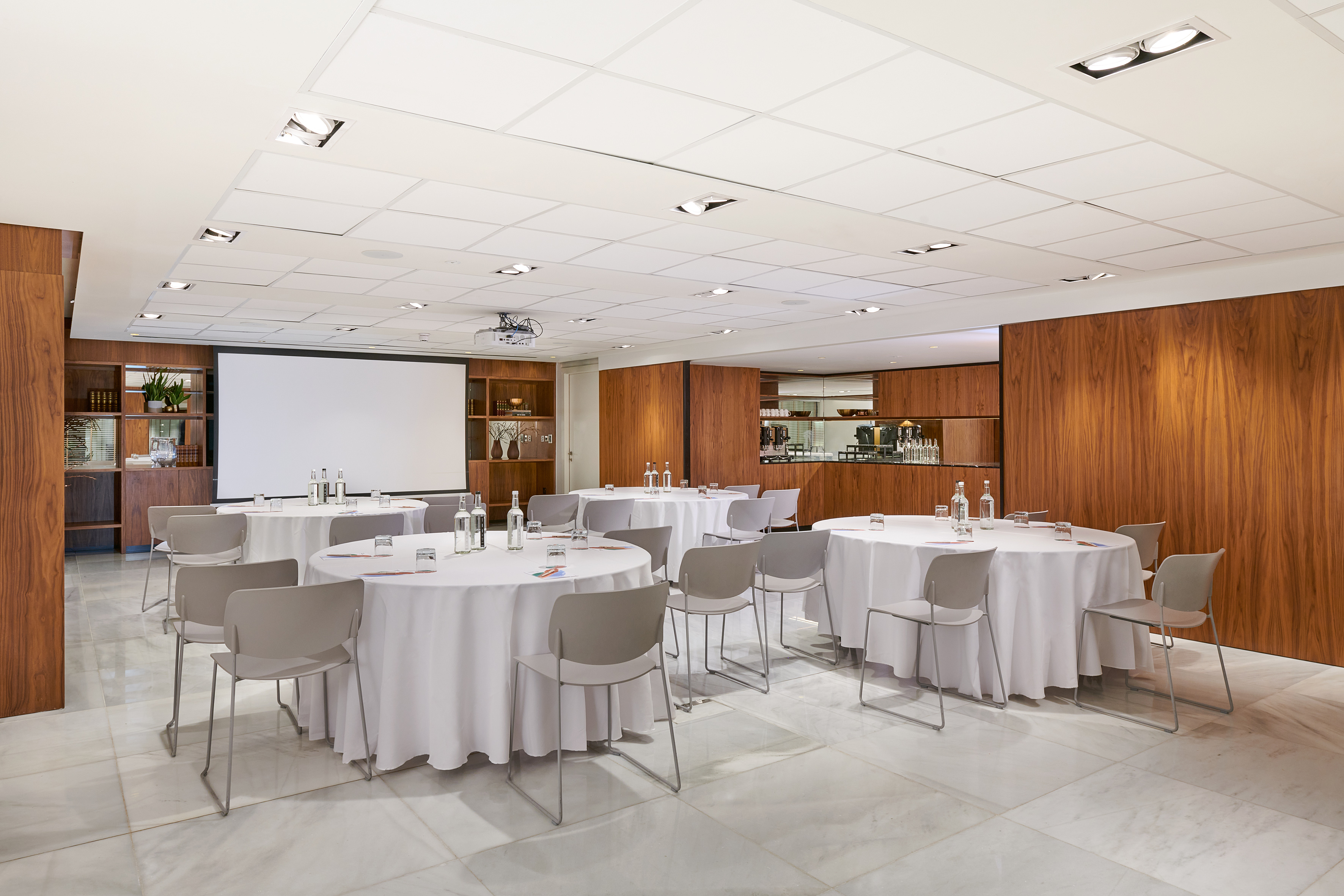 Modern meeting room with round tables, projector screen, and wood panels.