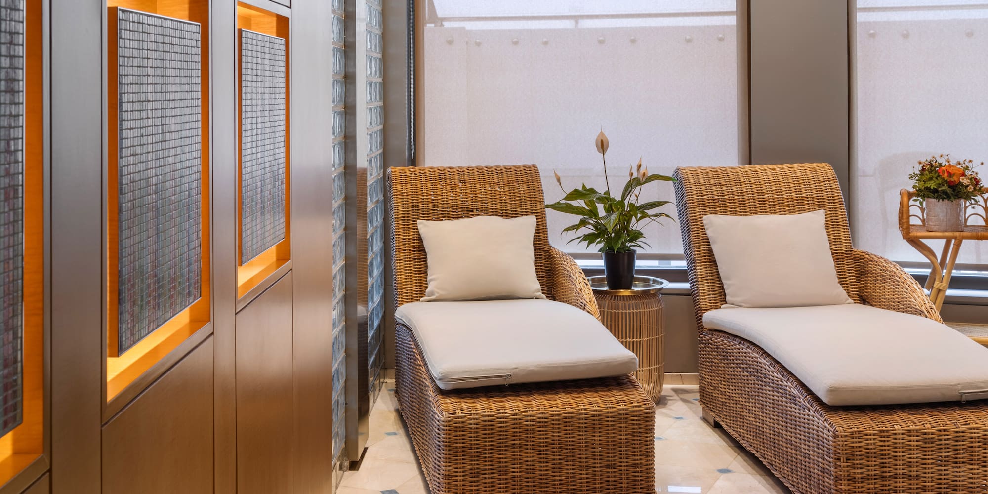 Serene hotel spa lounge with two wicker chaises, plants, and wood details.