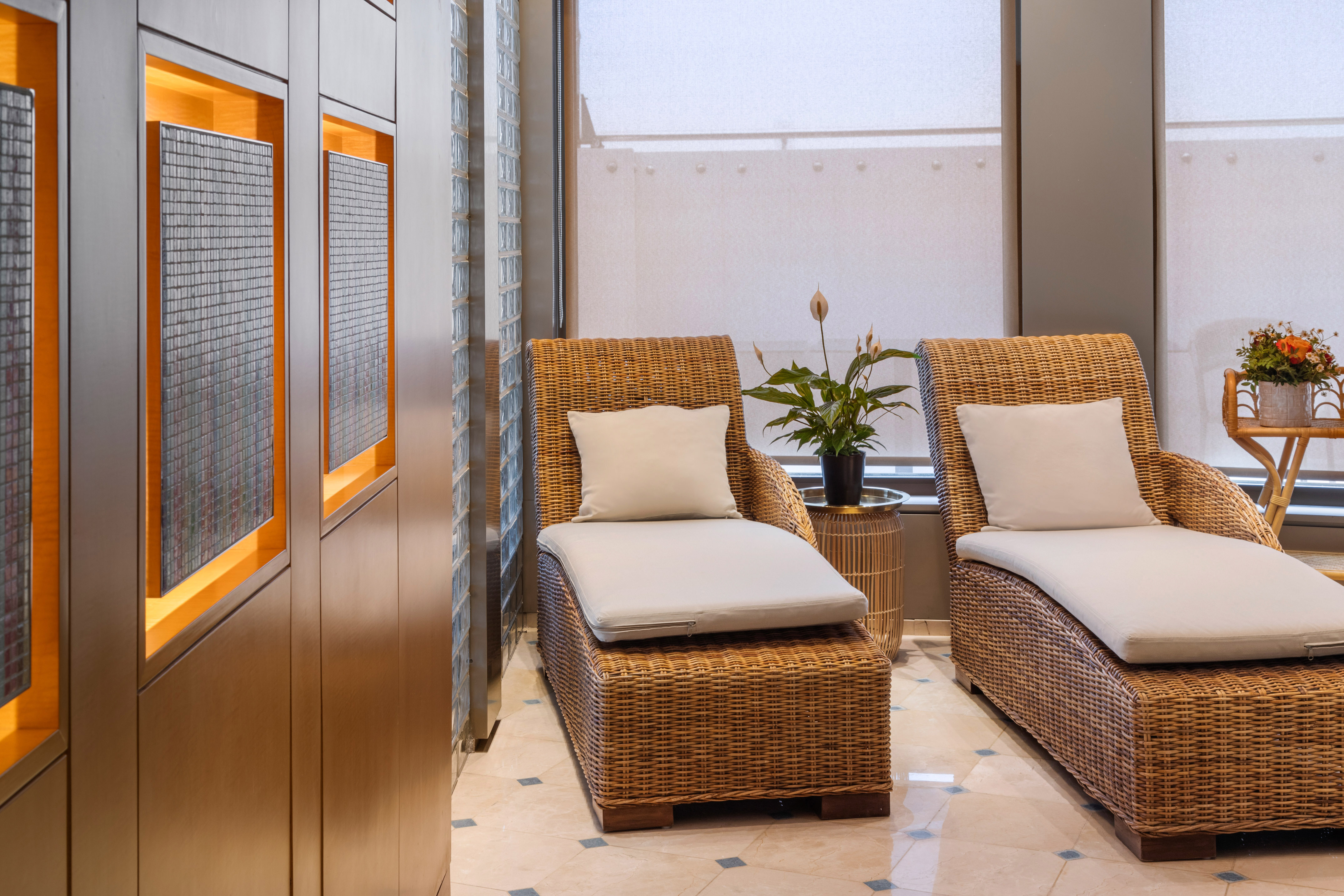 Serene hotel spa lounge with two wicker chaises, plants, and wood details.