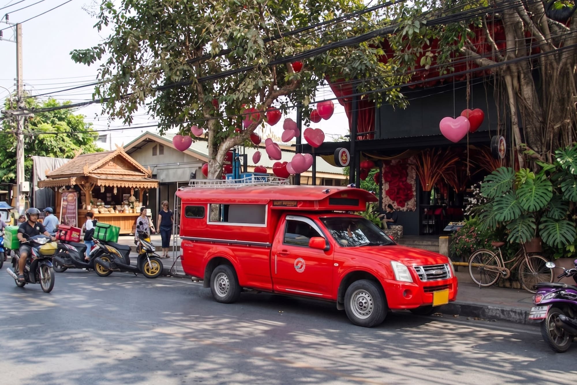 Red songthaew on a vibrant Thai street with heart decorations and wooden stalls.