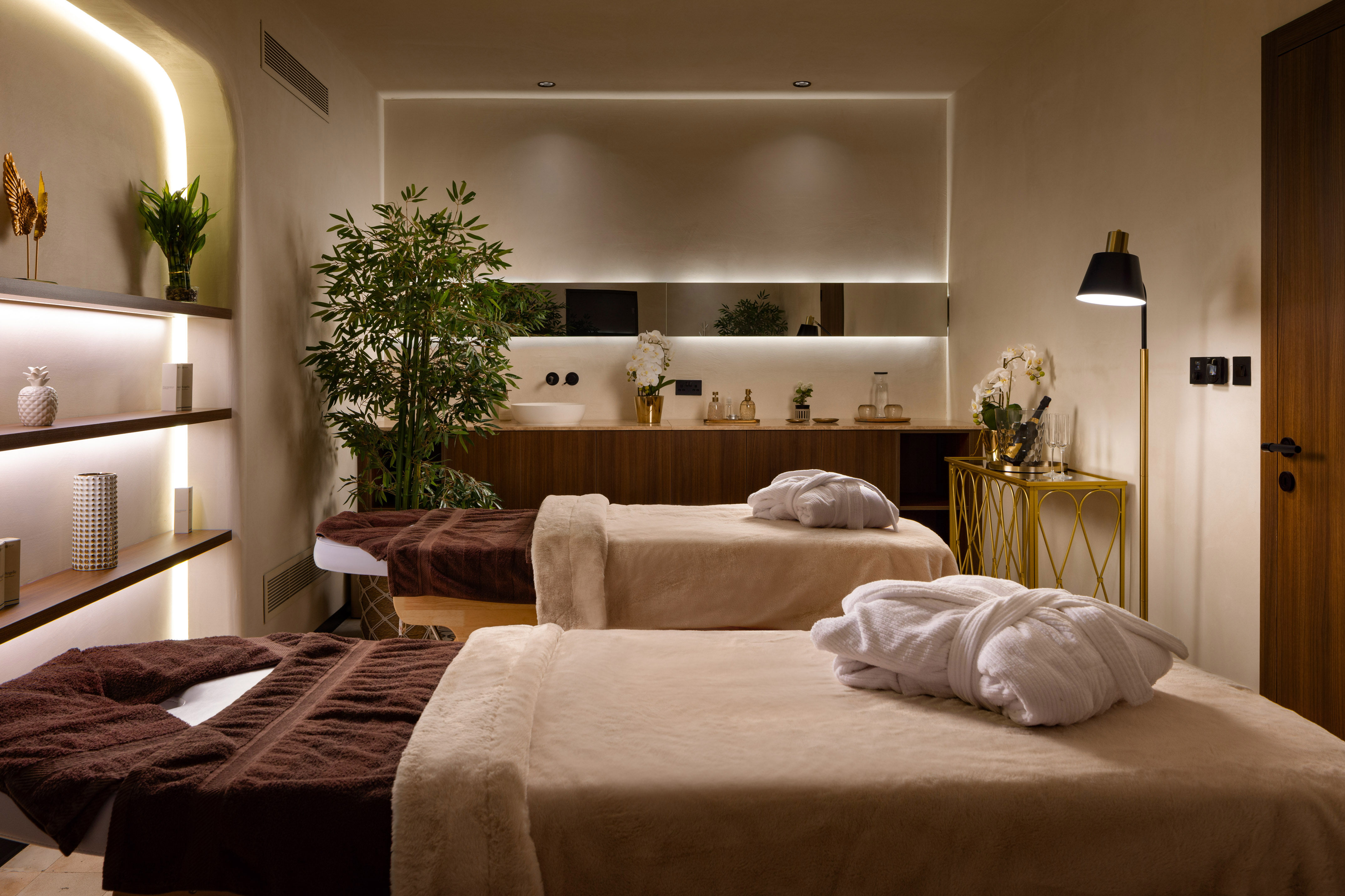 Serene spa room with two massage beds, white robes, and green plants.
