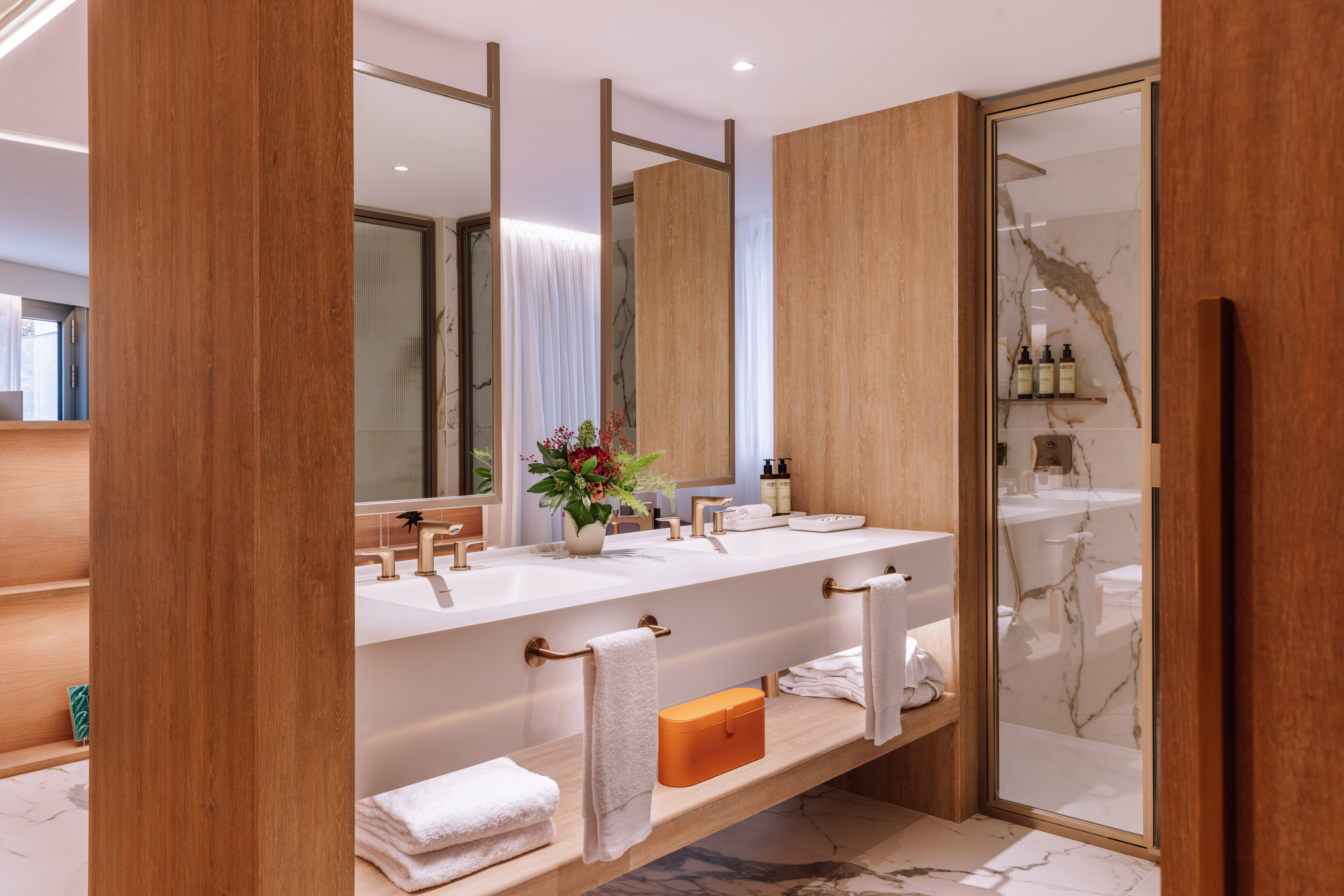 Modern double vanity bathroom with wood paneling, marble, and gold fixtures.