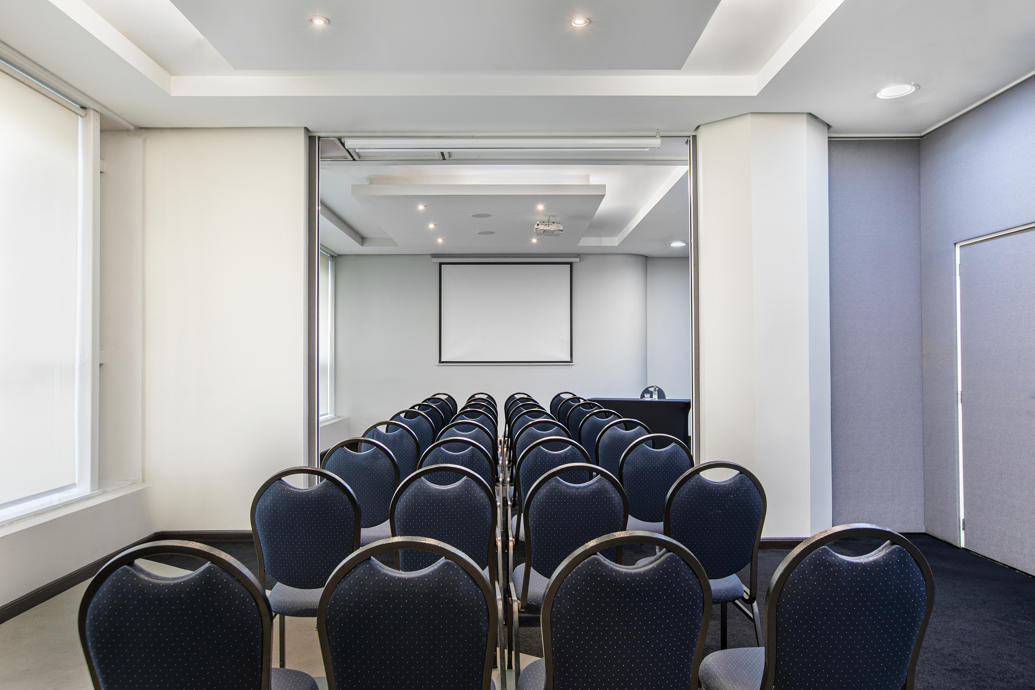 Empty modern conference room with rows of chairs and a projector screen.