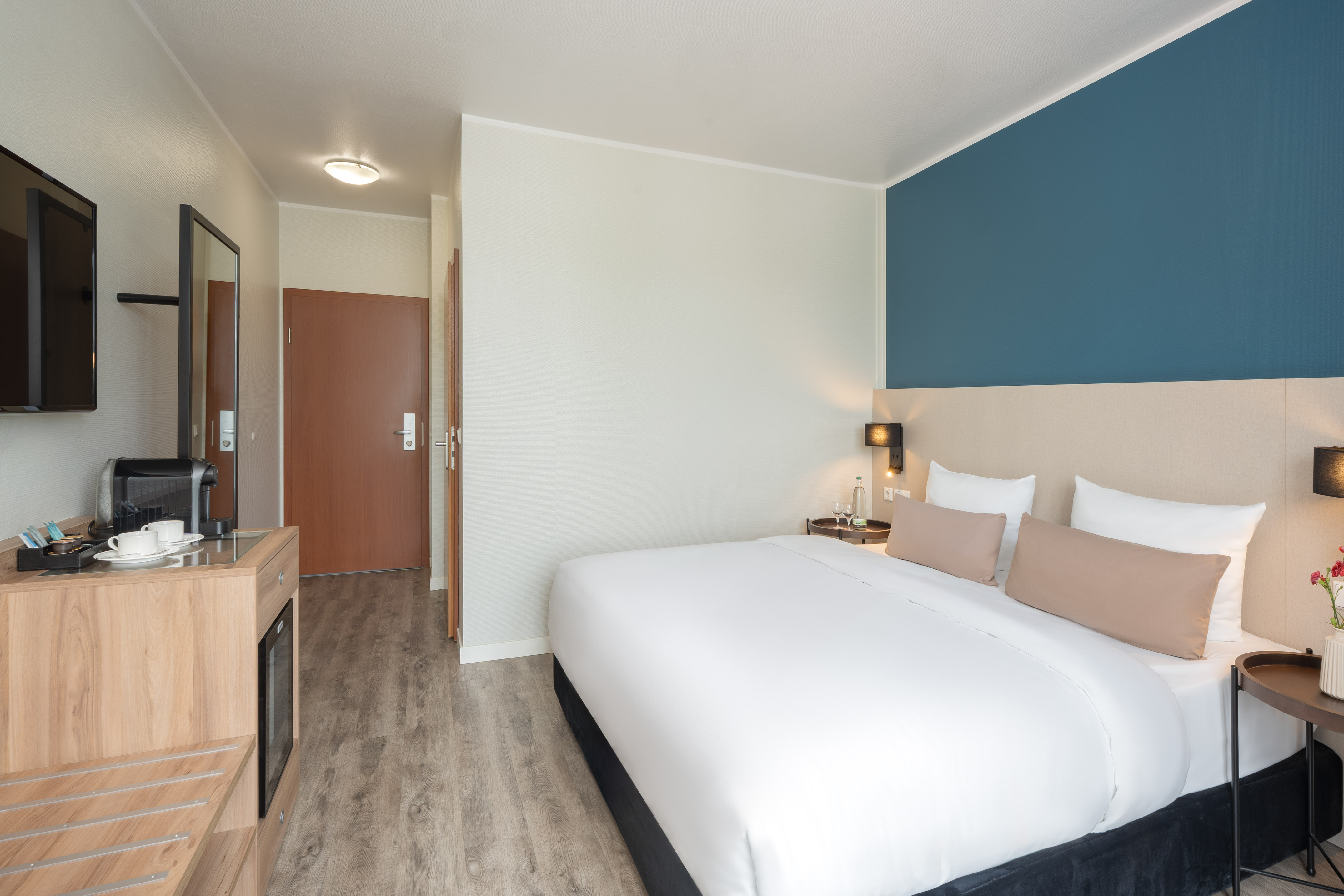 Comfortable hotel room with large bed, blue accent wall, coffee machine, and TV.