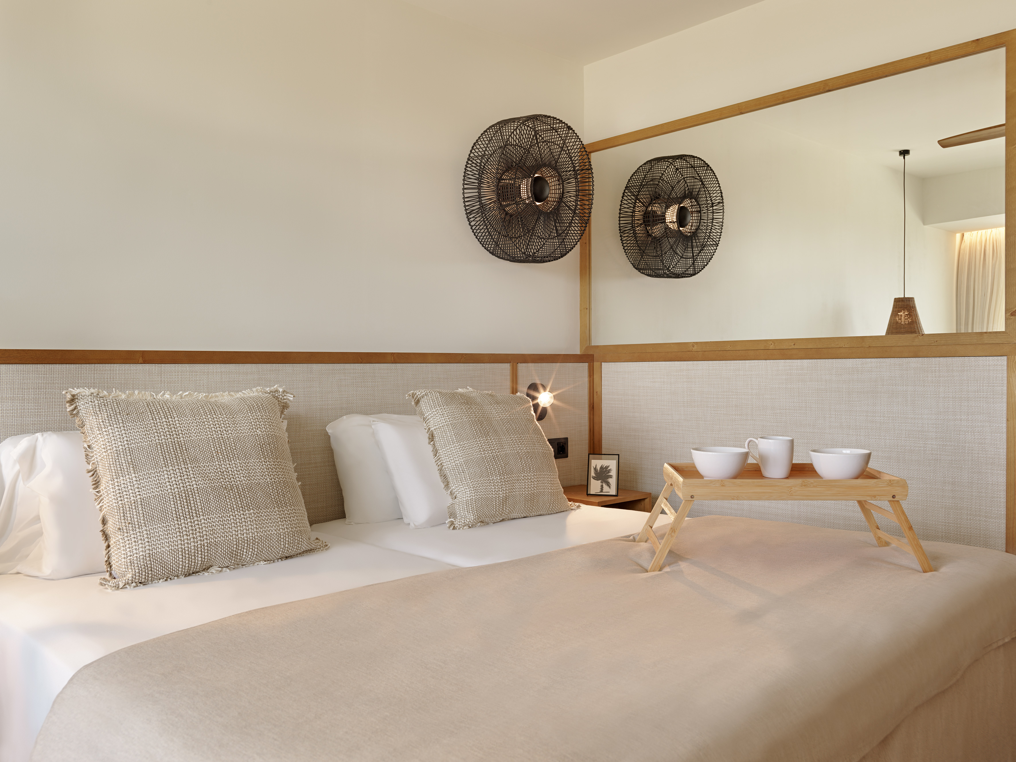 Contemporary hotel room with double bed, breakfast tray, and rattan decor.