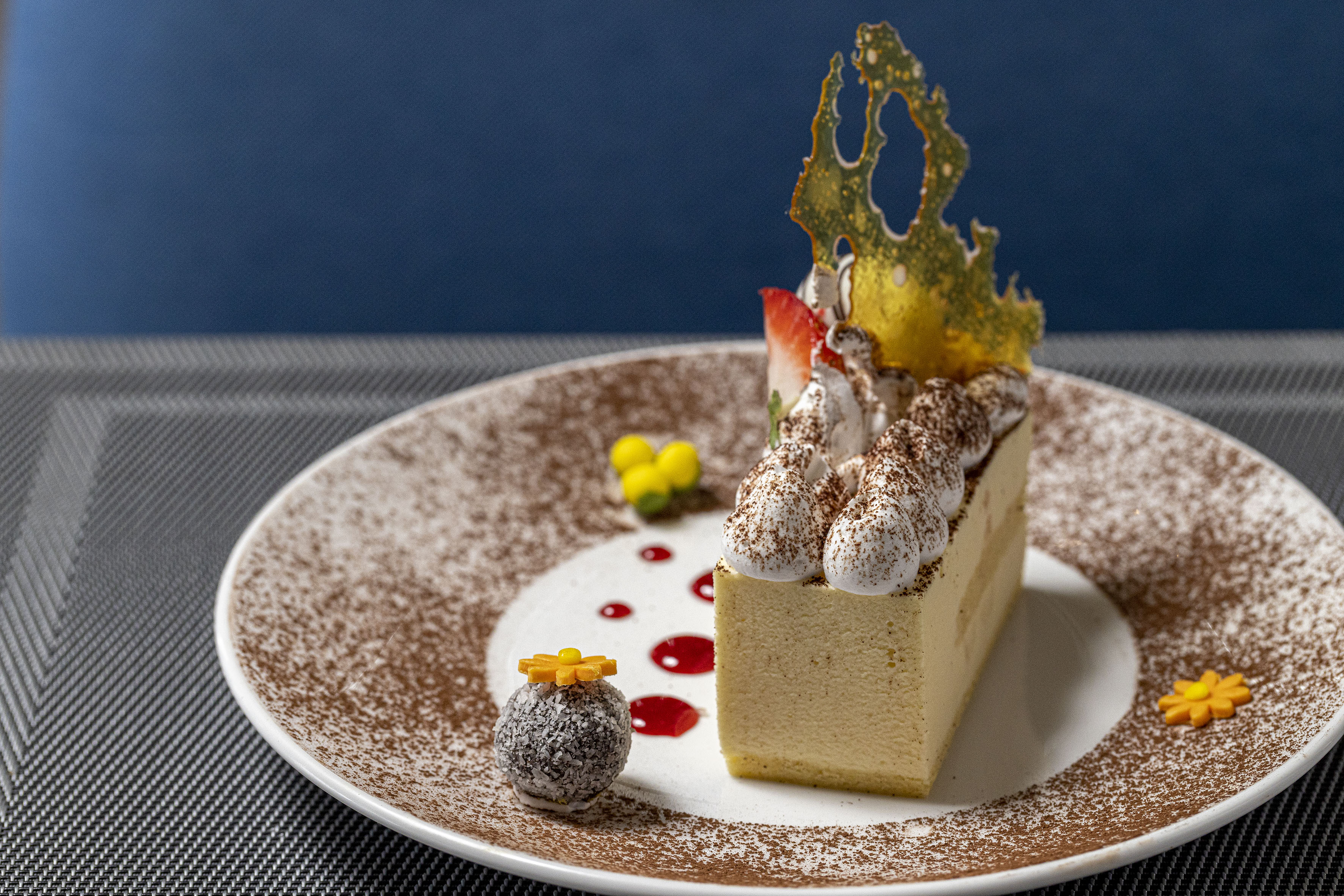 Cheesecake slice with whipped cream, strawberry, cocoa, and caramel art.