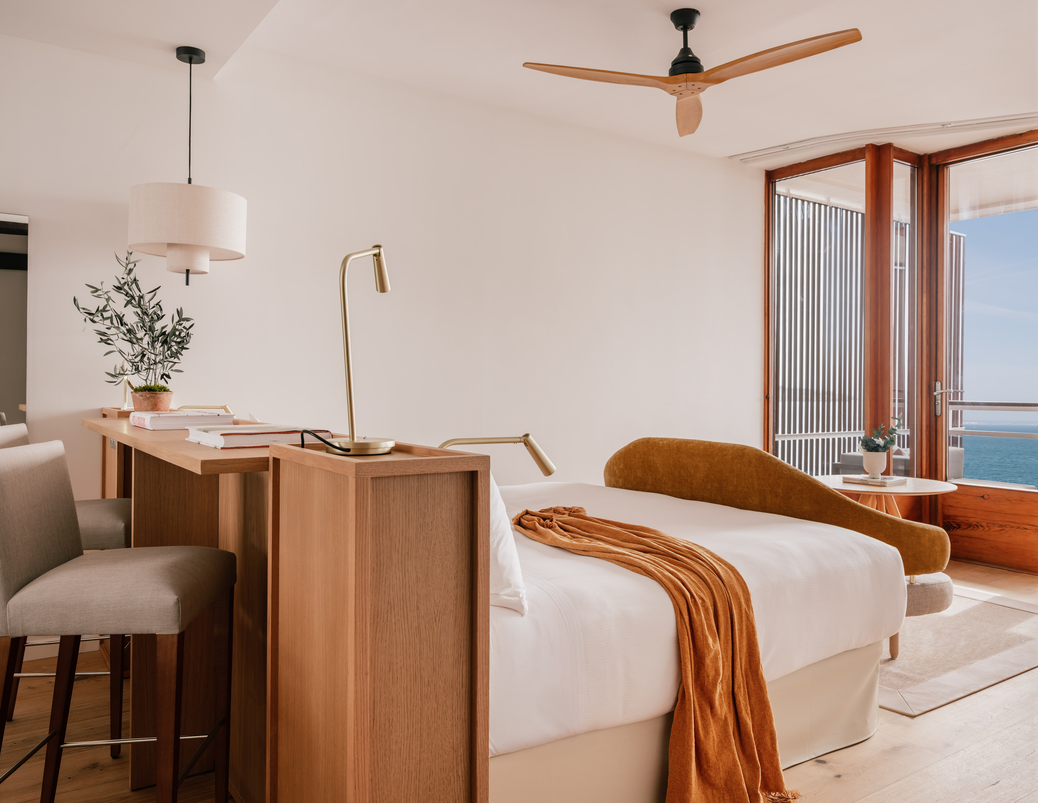 Coastal hotel room with ocean view, wooden balcony, modern bed, and desk.