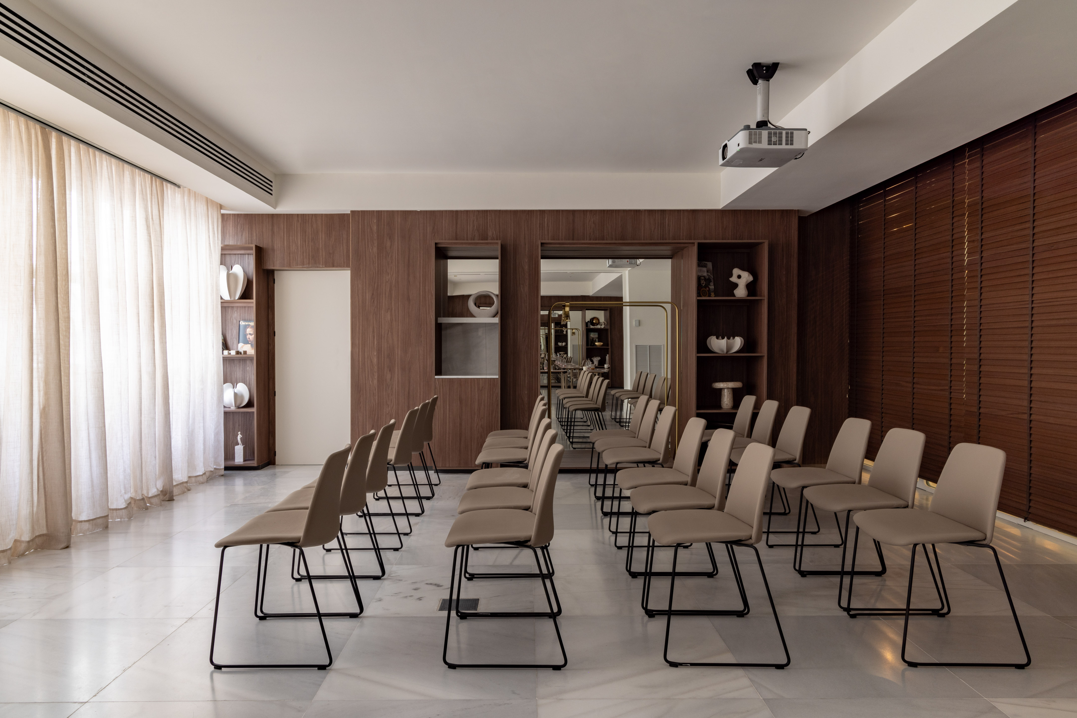 Modern conference room with beige chairs, ceiling projector, wood panels, marble floor.