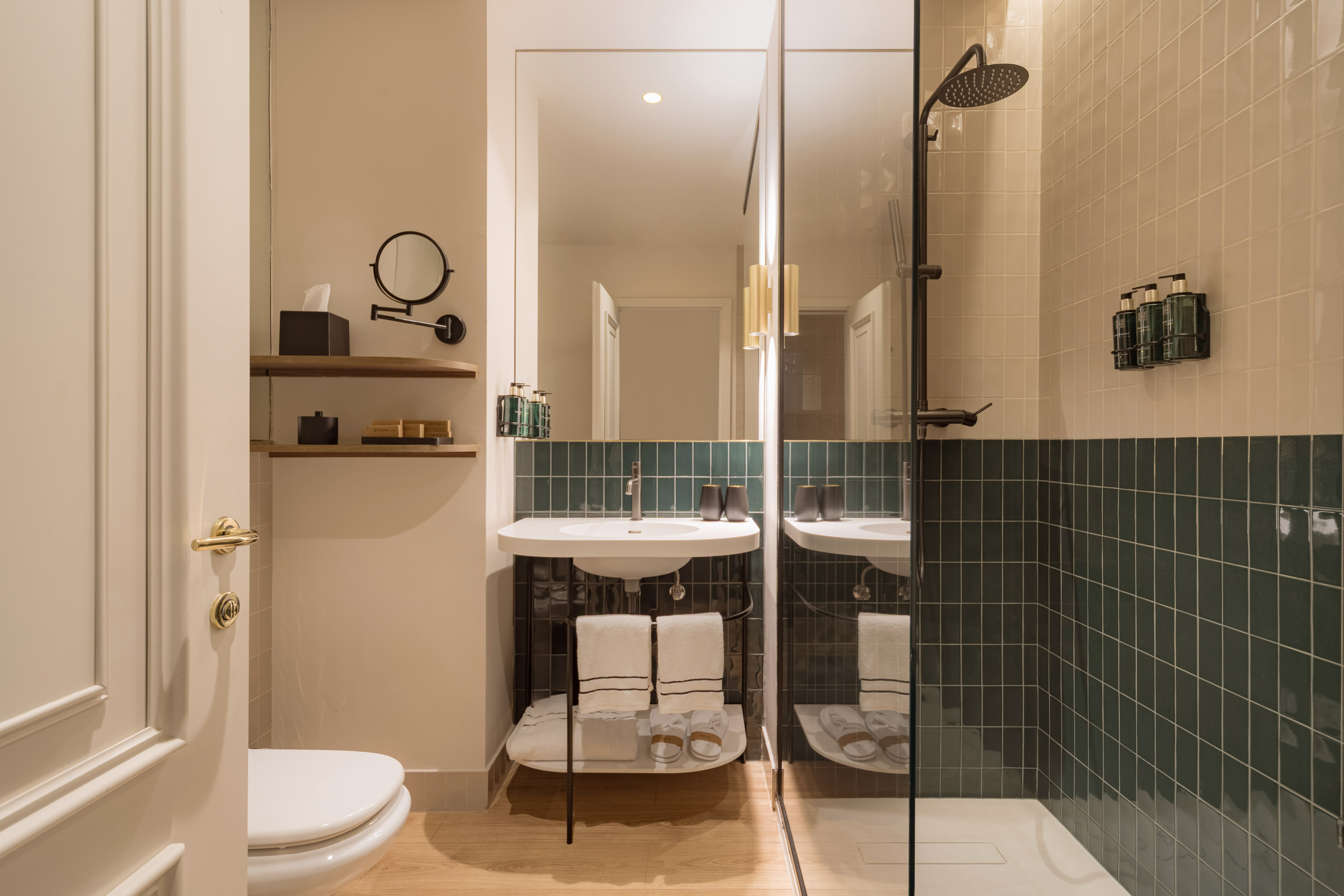 Modern hotel bathroom with green subway tiles, white sink, shower, and wooden floor.