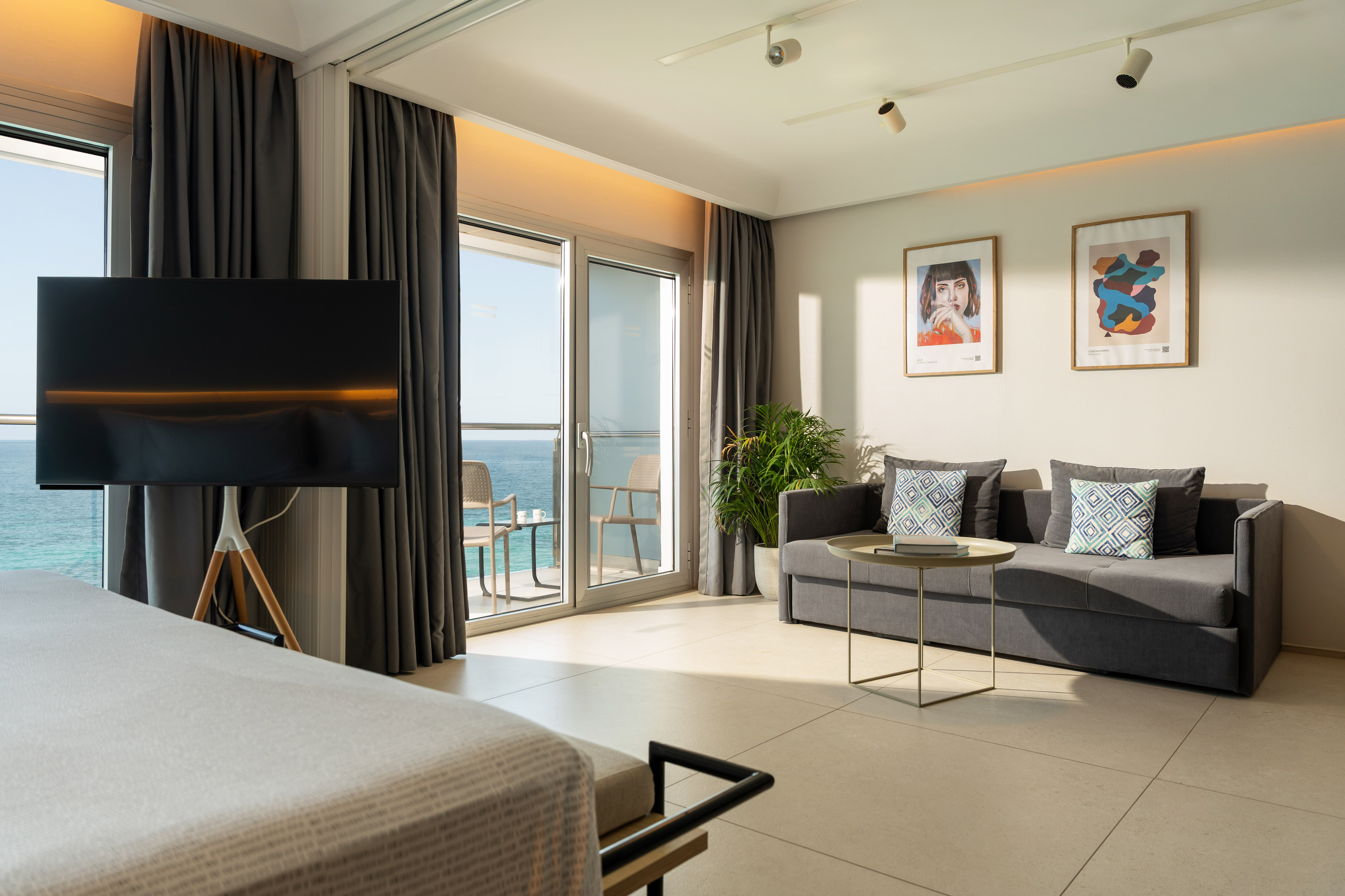 Modern ocean view hotel suite with balcony, sofa, TV, and contemporary decor.