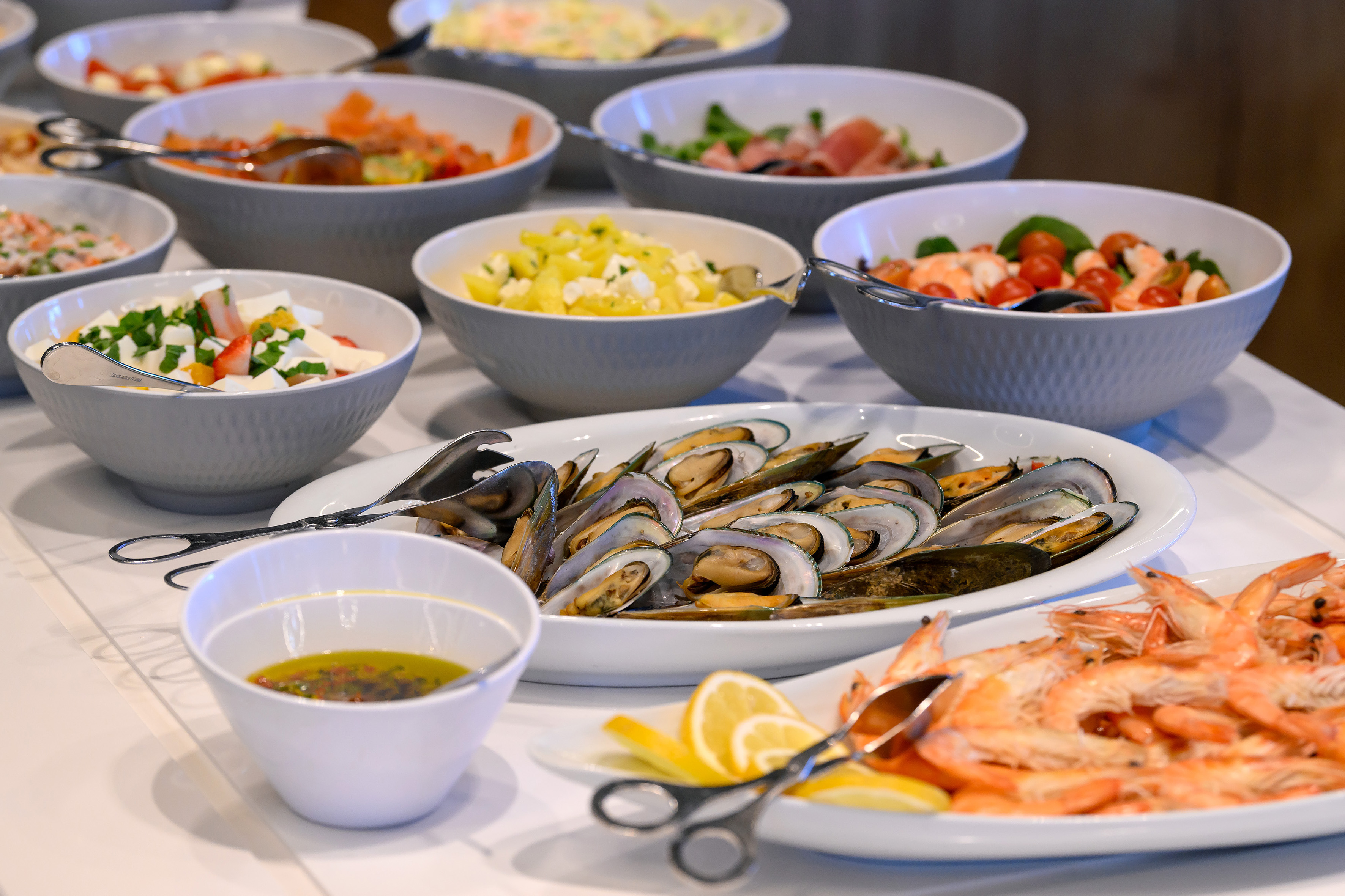 Buffet table with fresh salads, steamed mussels, and cooked shrimp.