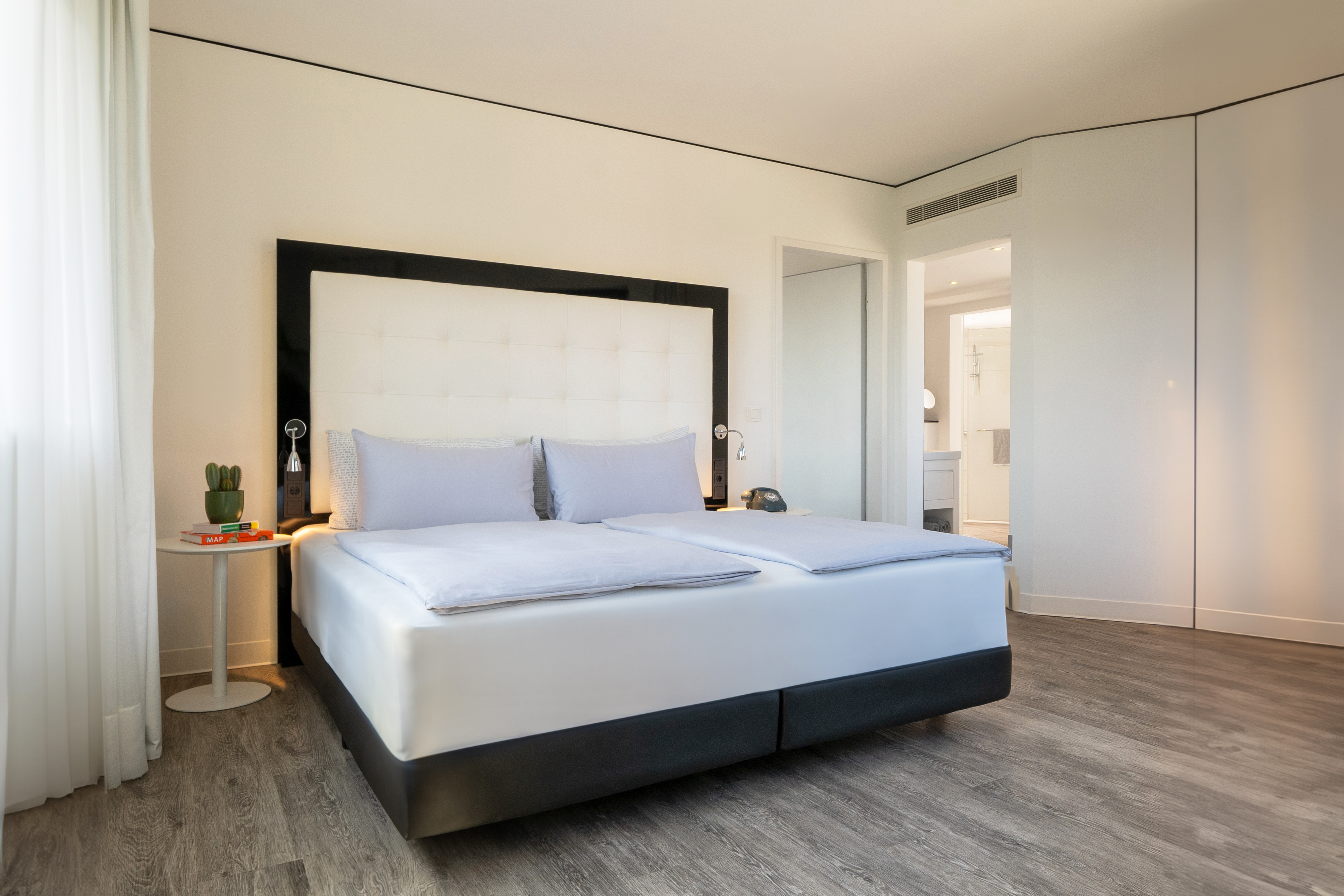Bright contemporary hotel room with white bed, light wood floor.