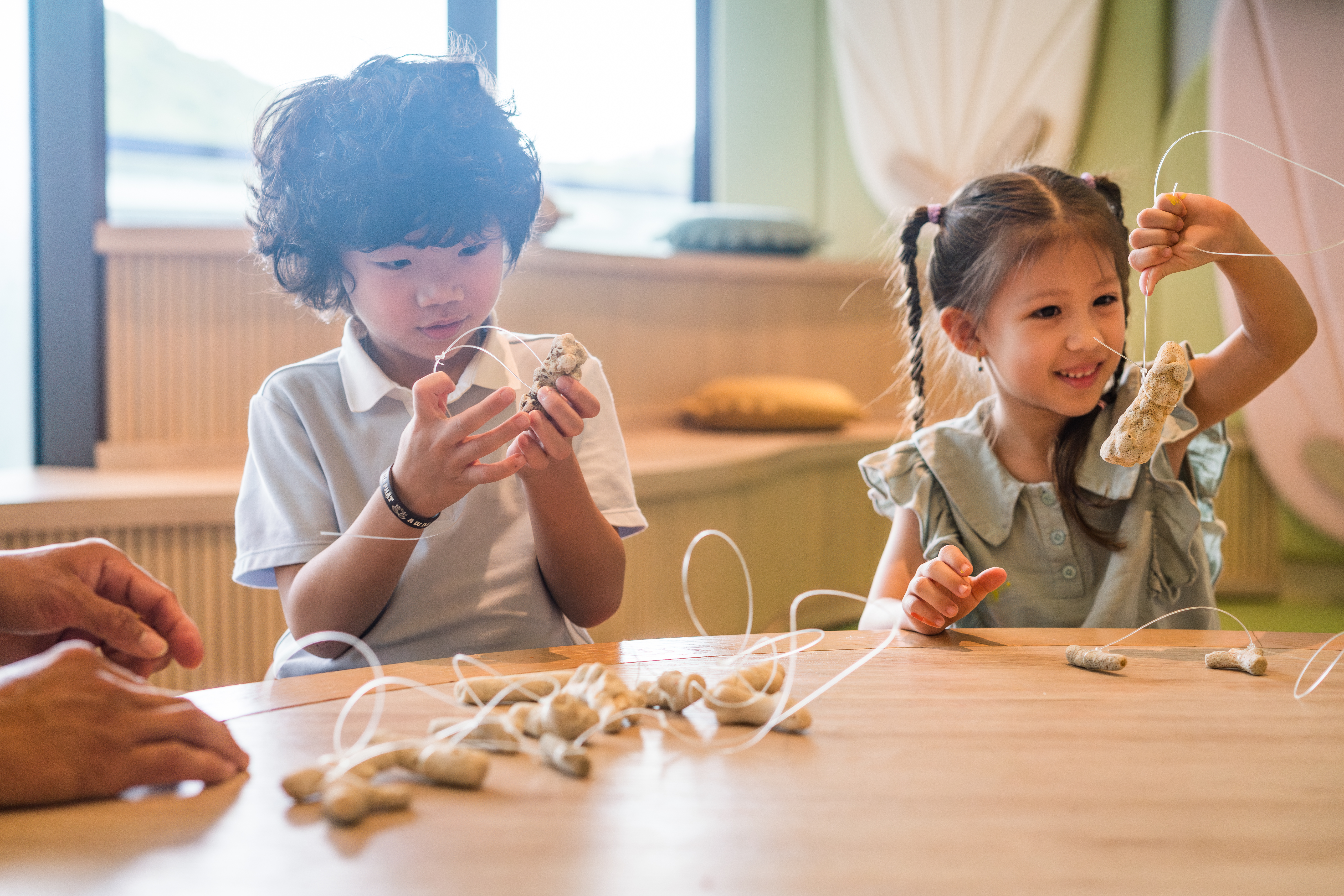 Niño y niña haciendo manualidades con materiales naturales en mesa.