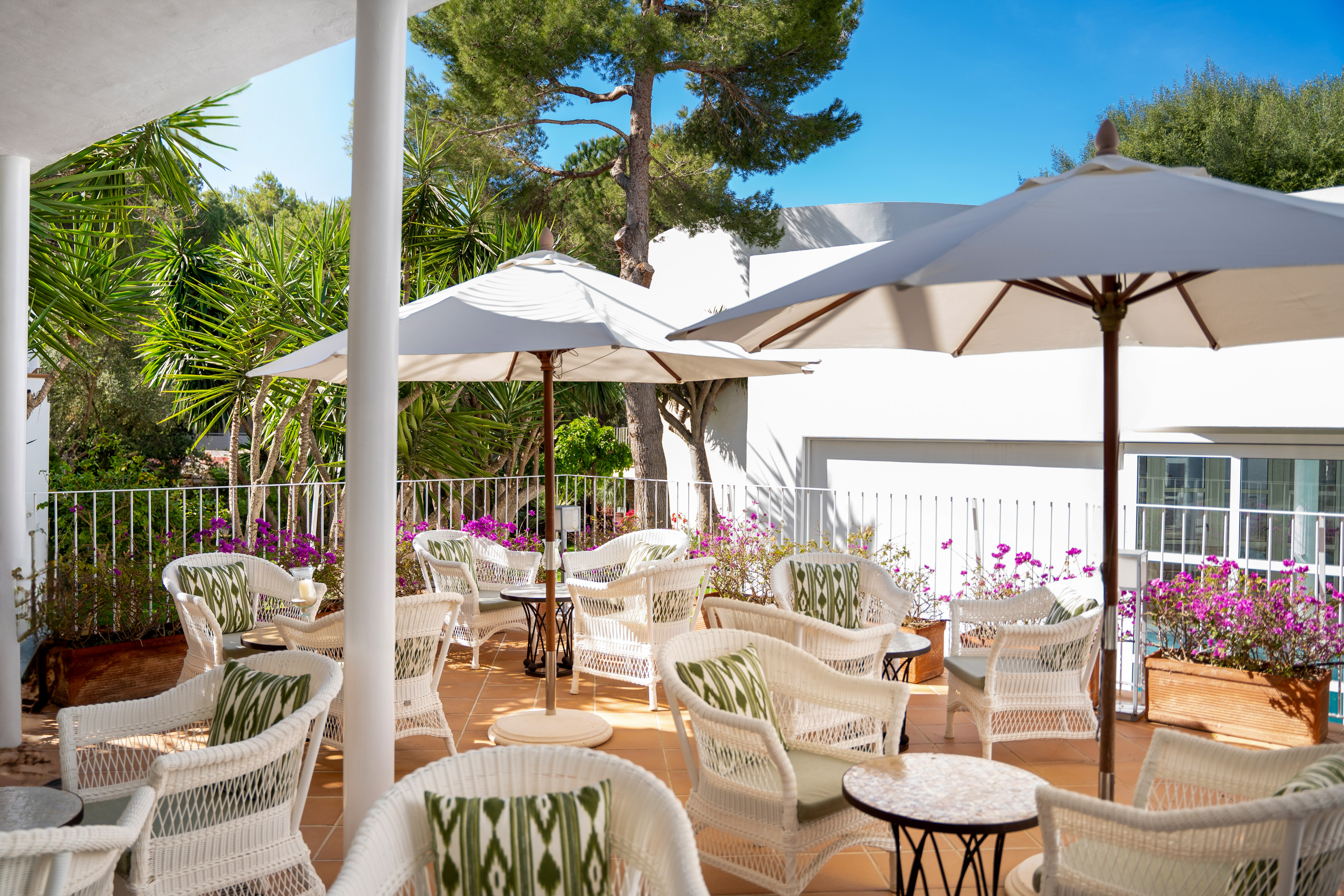 Resort patio with white wicker chairs, green cushions, umbrellas, and flowers.