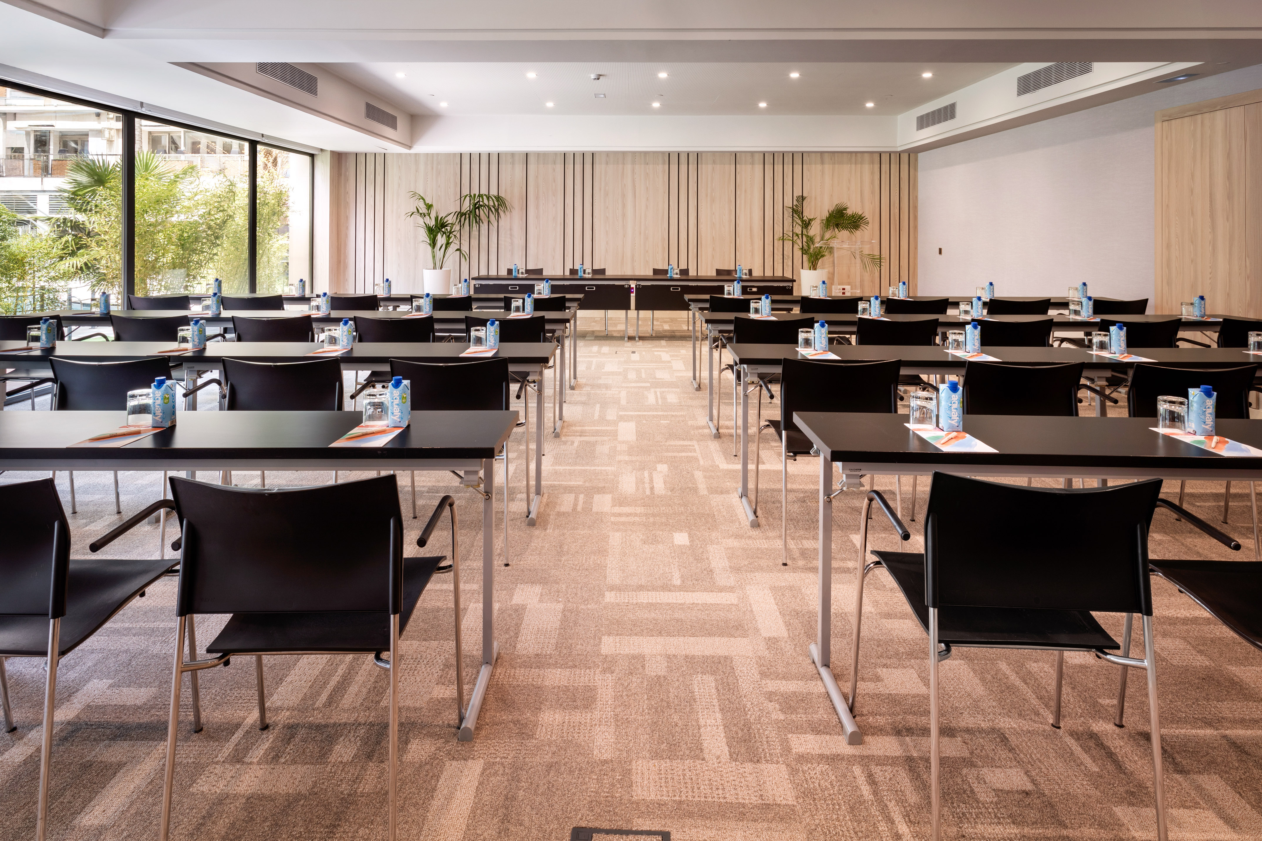 Modern conference room with black tables, chairs, water bottles, and large windows.
