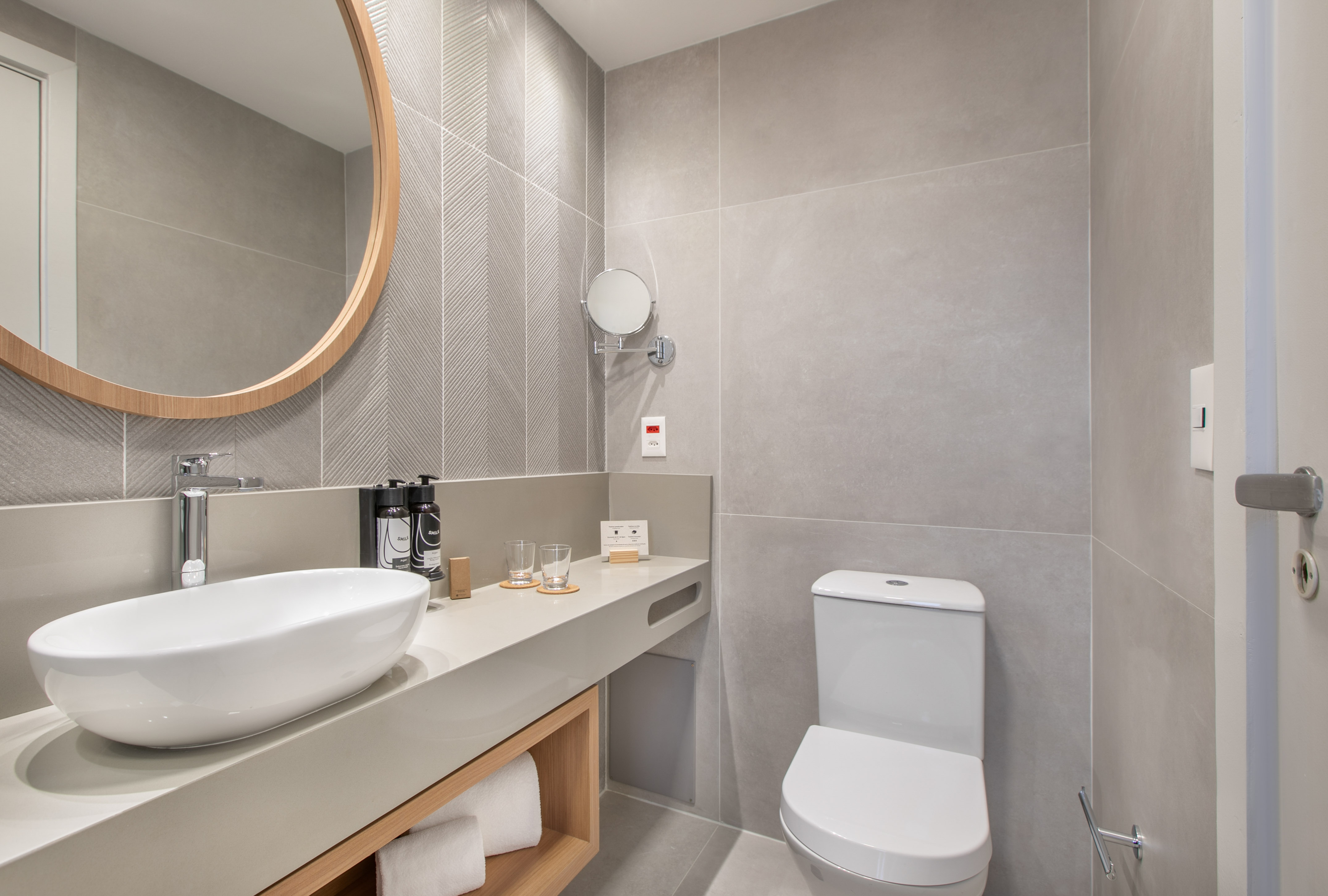 Modern bathroom with gray tiles, white vessel sink, wood mirror, and toilet.