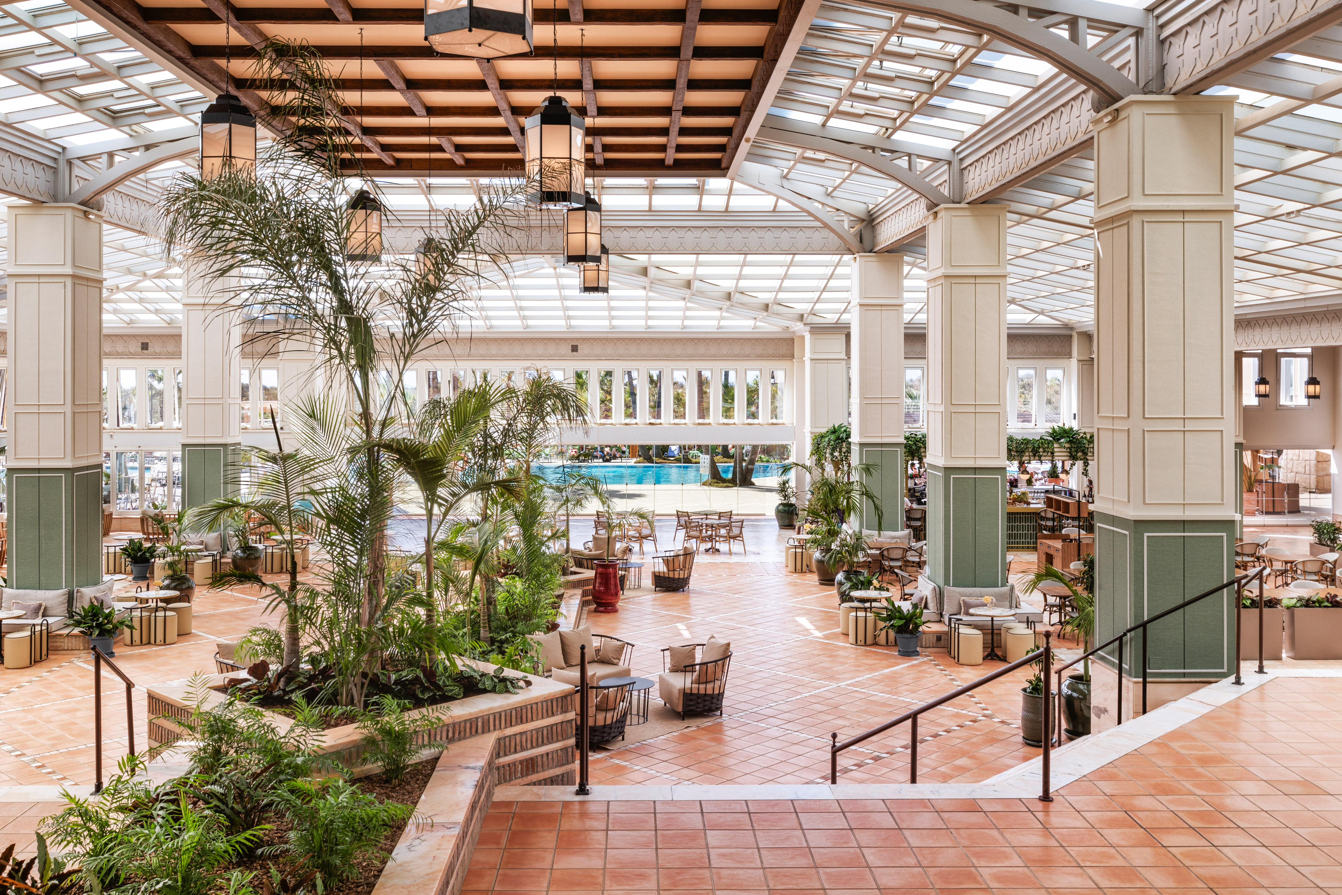 Resort lobby with indoor palms, lounge seating, terracotta tiles, and outdoor pool view.
