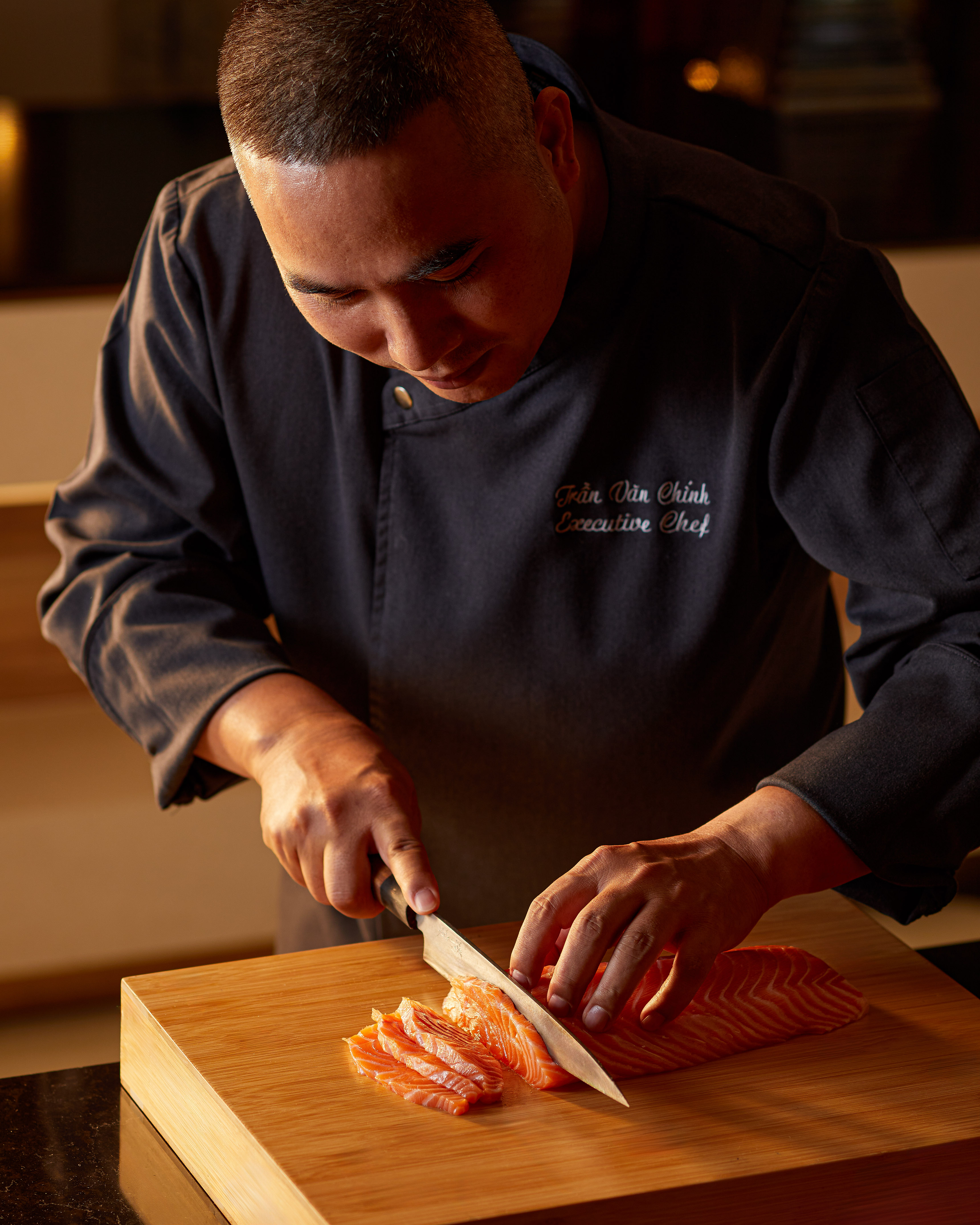 Executive chef slicing fresh salmon on a wooden board.