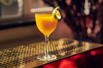 a glass of orange liquid with a lime wedge on a metal surface