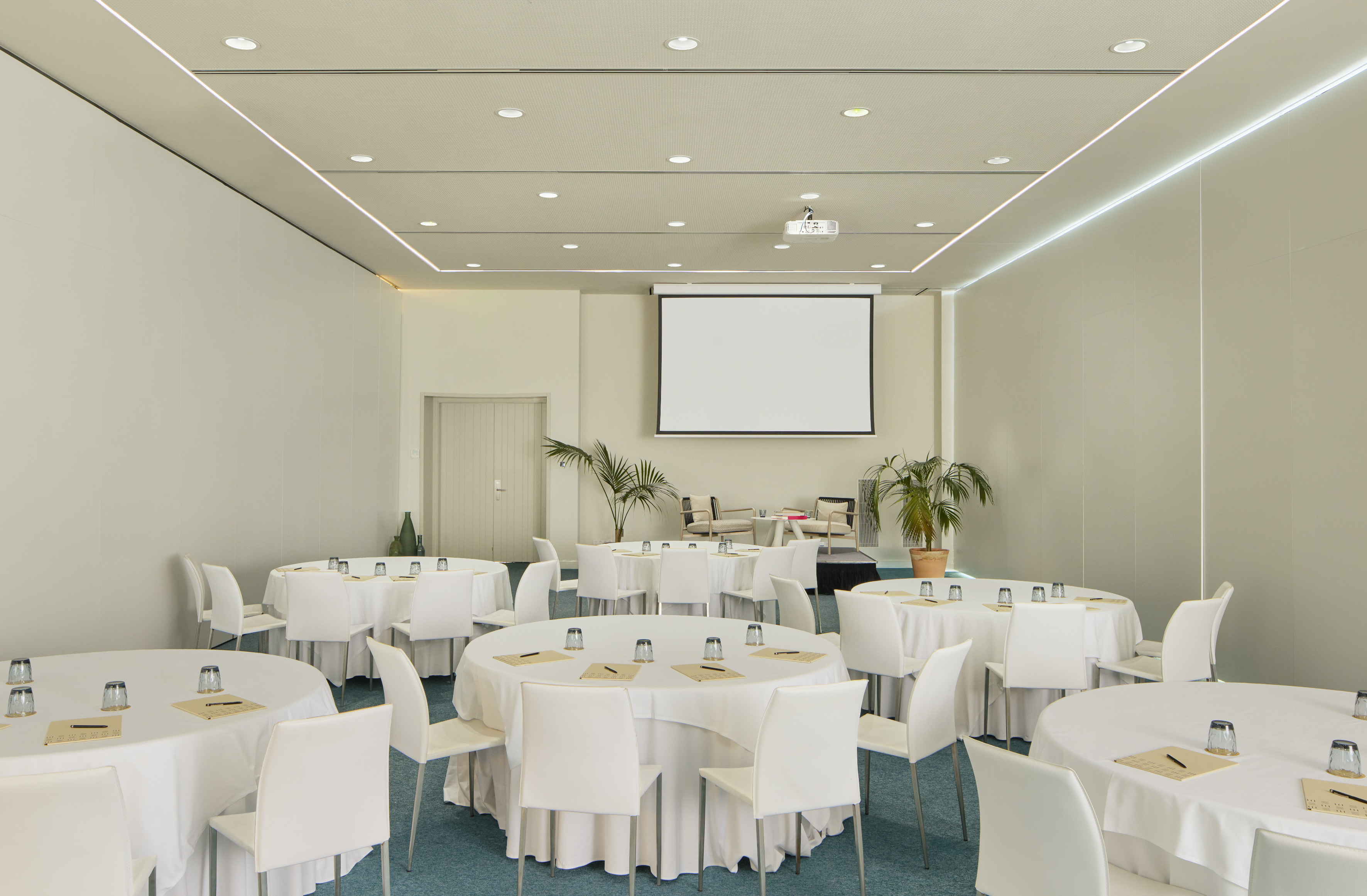 Empty modern conference room with round tables, white chairs, and projector screen.