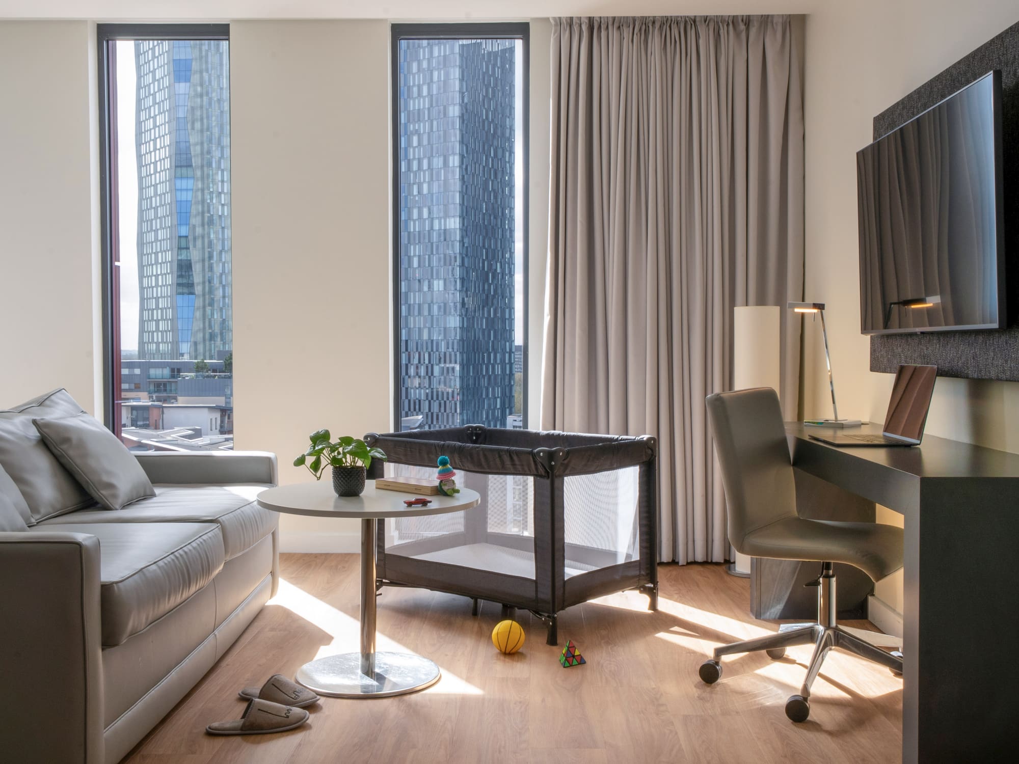 Modern baby-friendly apartment suite with sofa, workspace, and city view.