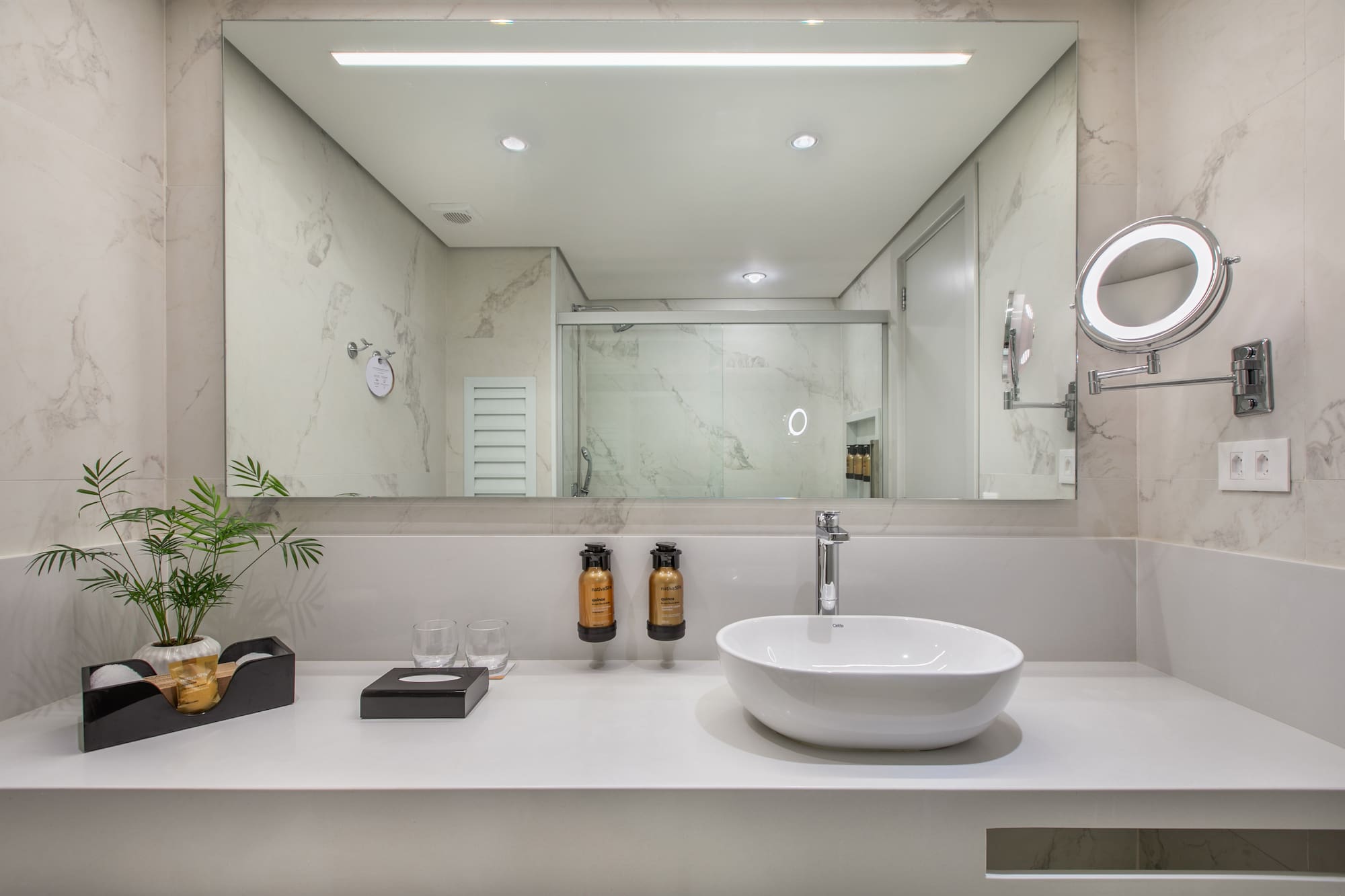 Modern bathroom vanity with white vessel sink, marble walls, and lighted mirror.