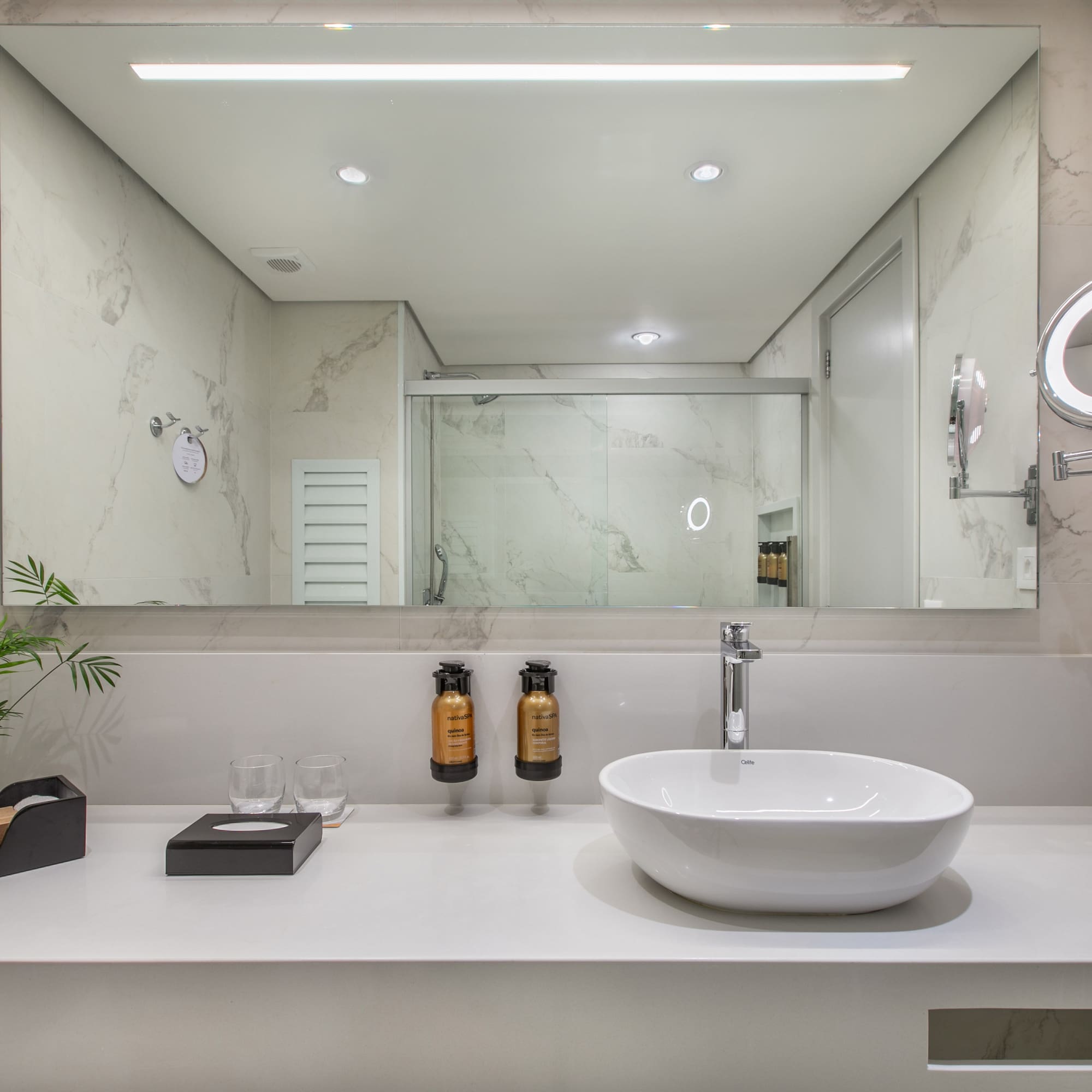 Modern bathroom vanity with white vessel sink, marble walls, and lighted mirror.