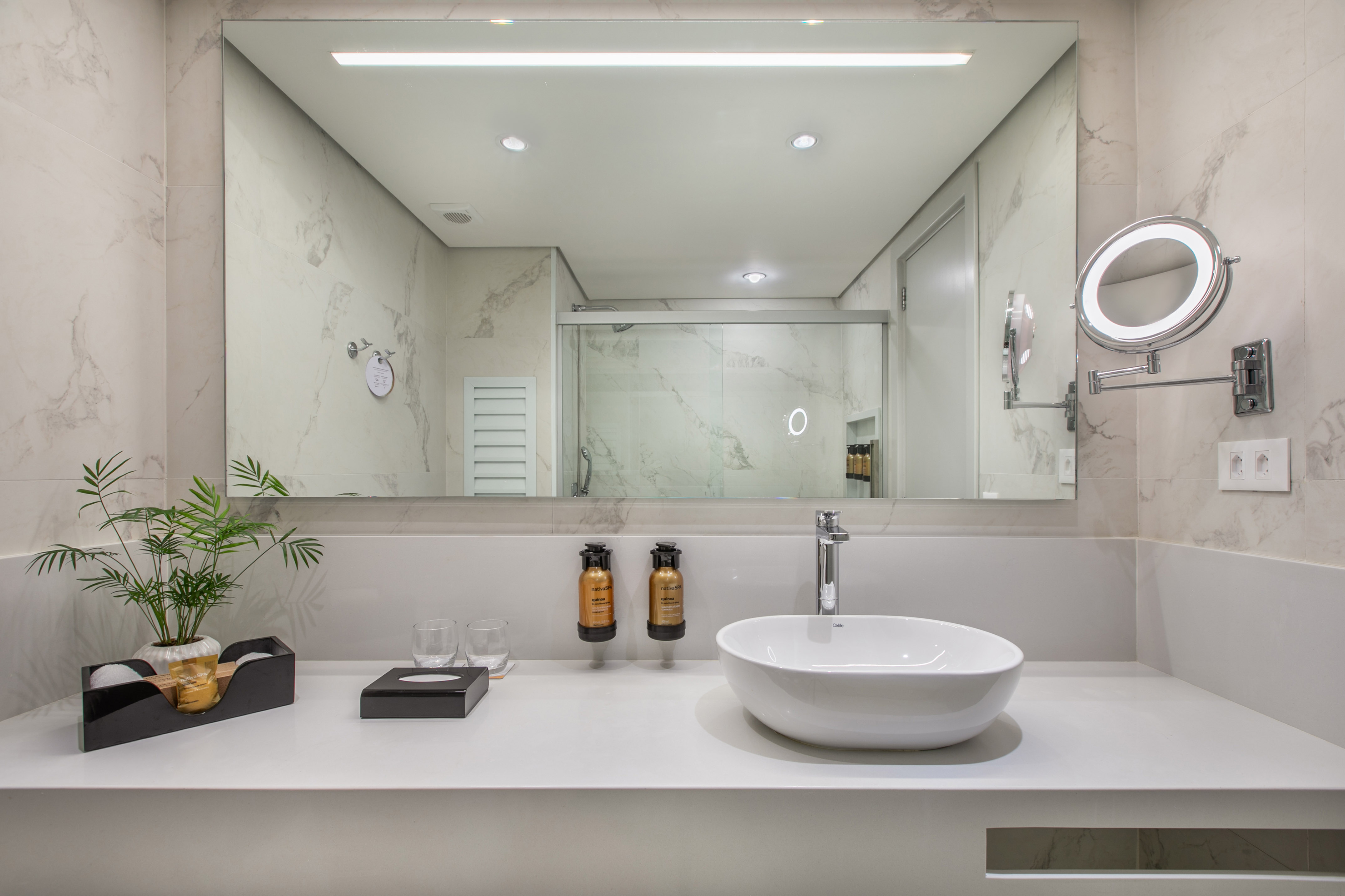 Modern bathroom vanity with white vessel sink, marble walls, and lighted mirror.