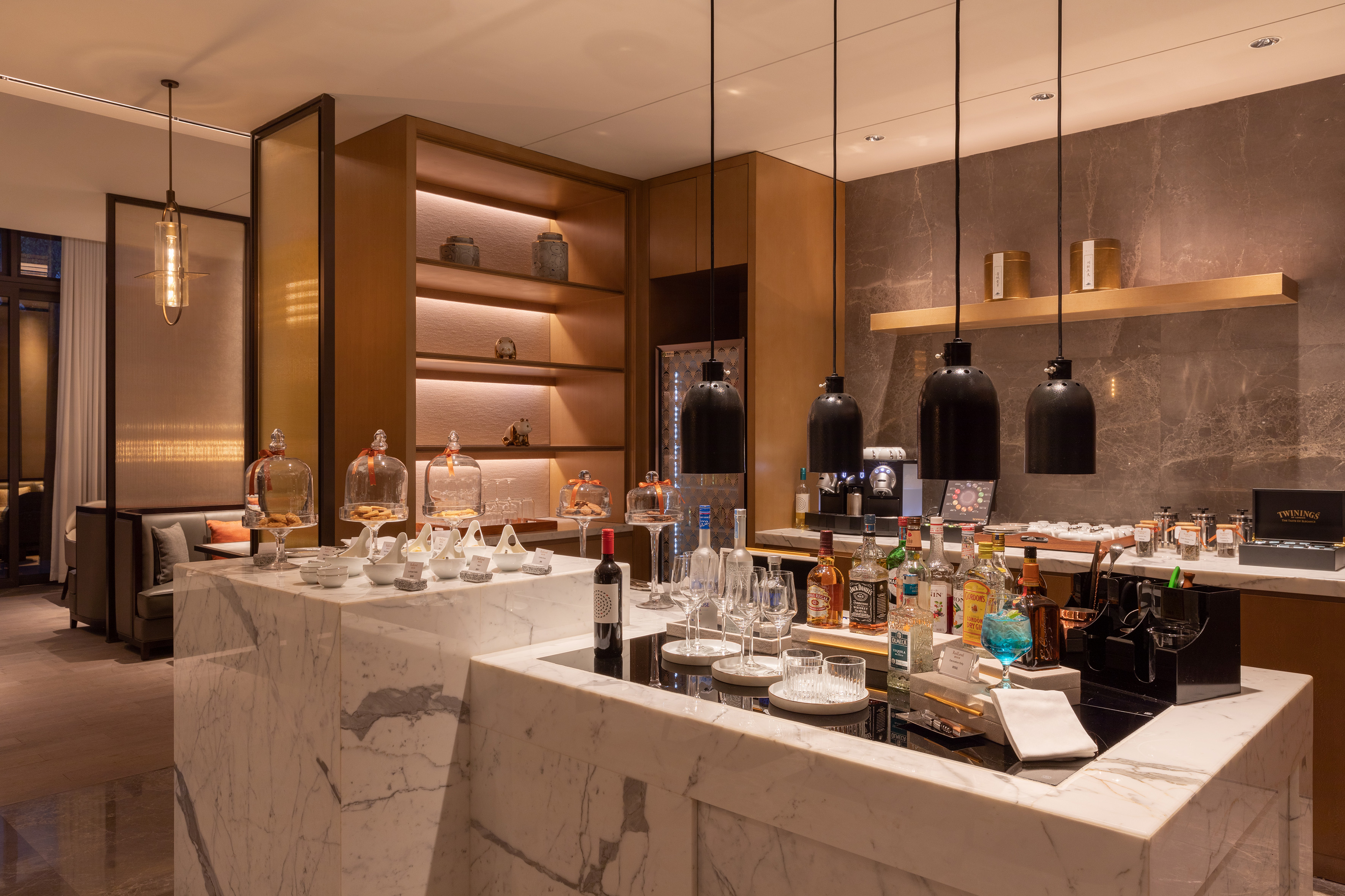 Chic hotel lounge bar with marble counter, drinks, snacks, and warm lighting.
