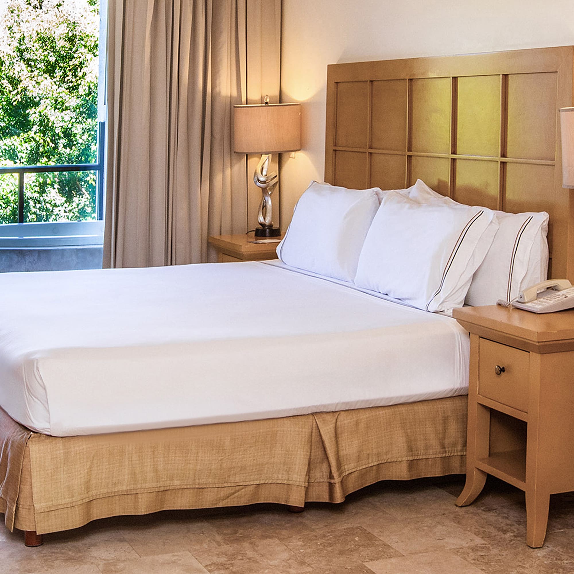 Hotel bedroom with king bed, nightstands, balcony spa tub, and green view.