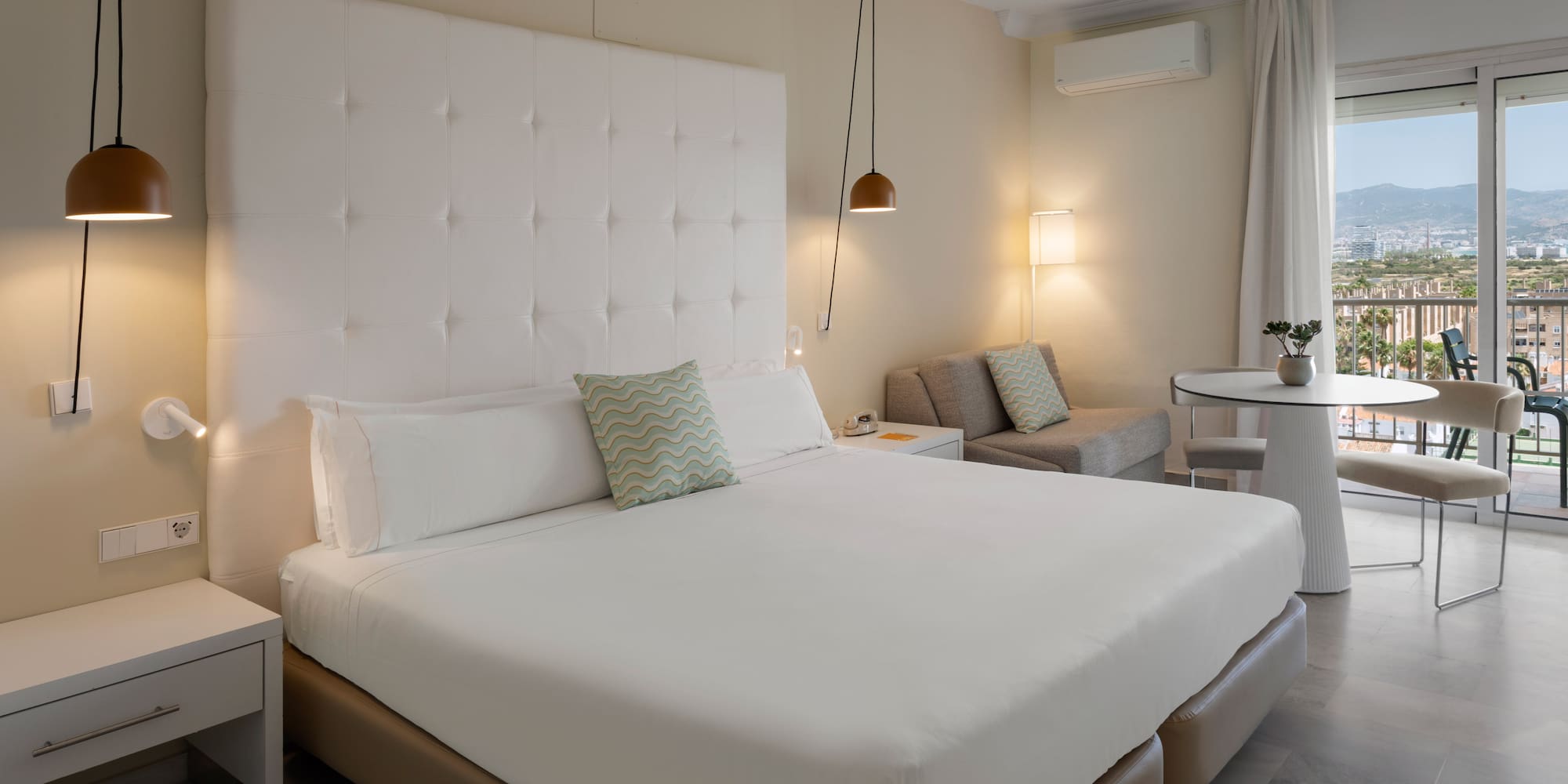 Suite de hotel moderna con cama doble, área de estar y balcón con vistas.
