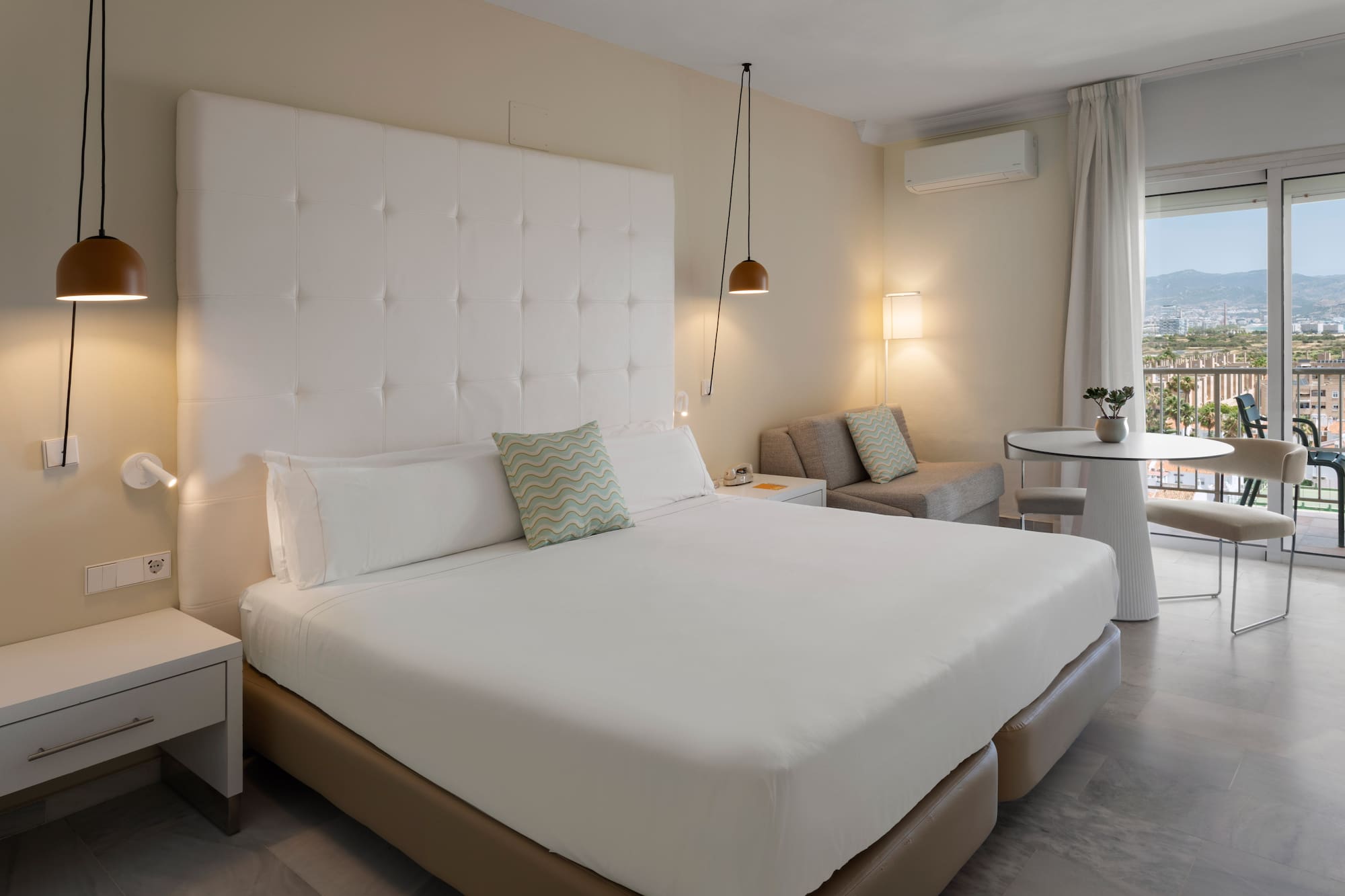 Suite de hotel moderna con cama doble, área de estar y balcón con vistas.