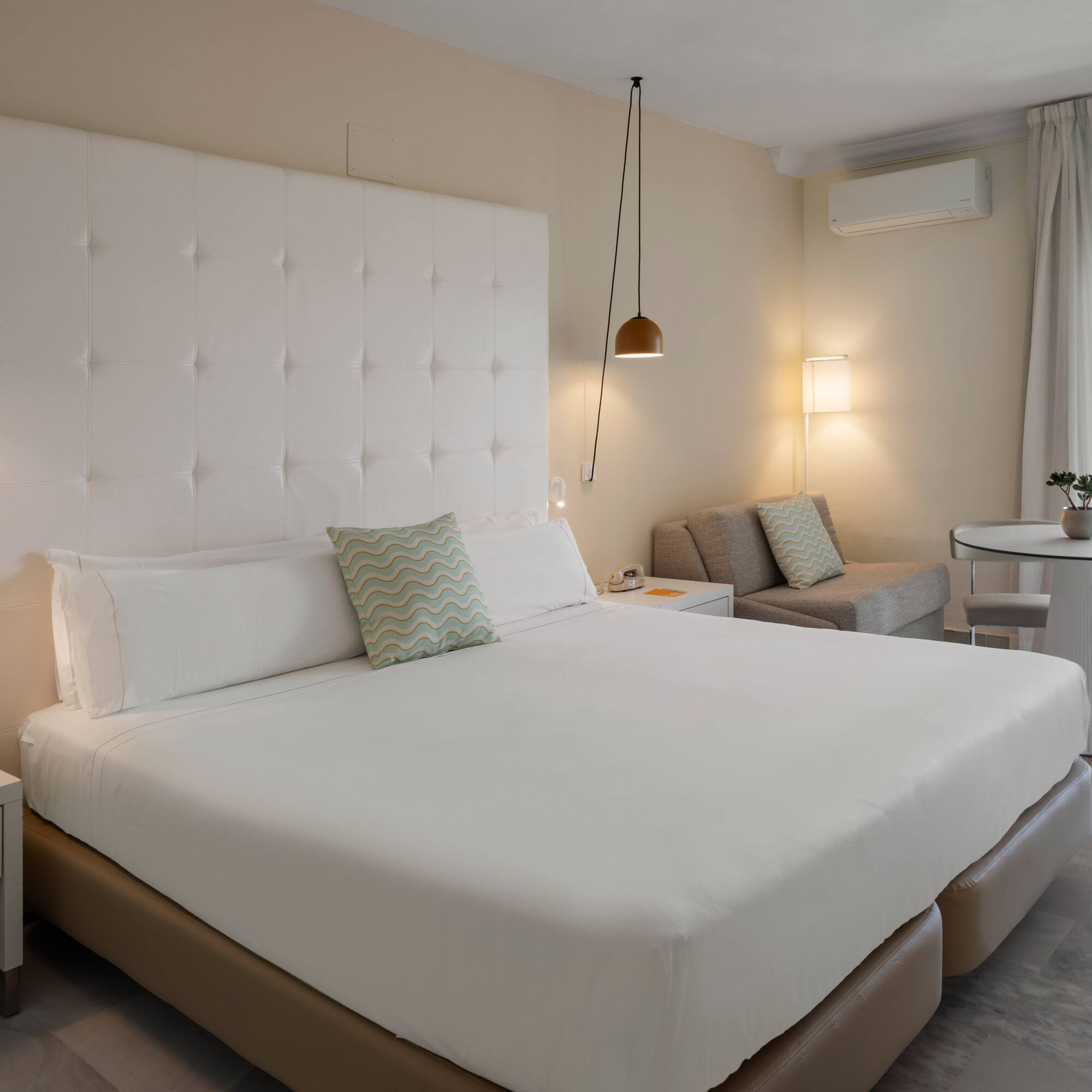 Suite de hotel moderna con cama doble, área de estar y balcón con vistas.