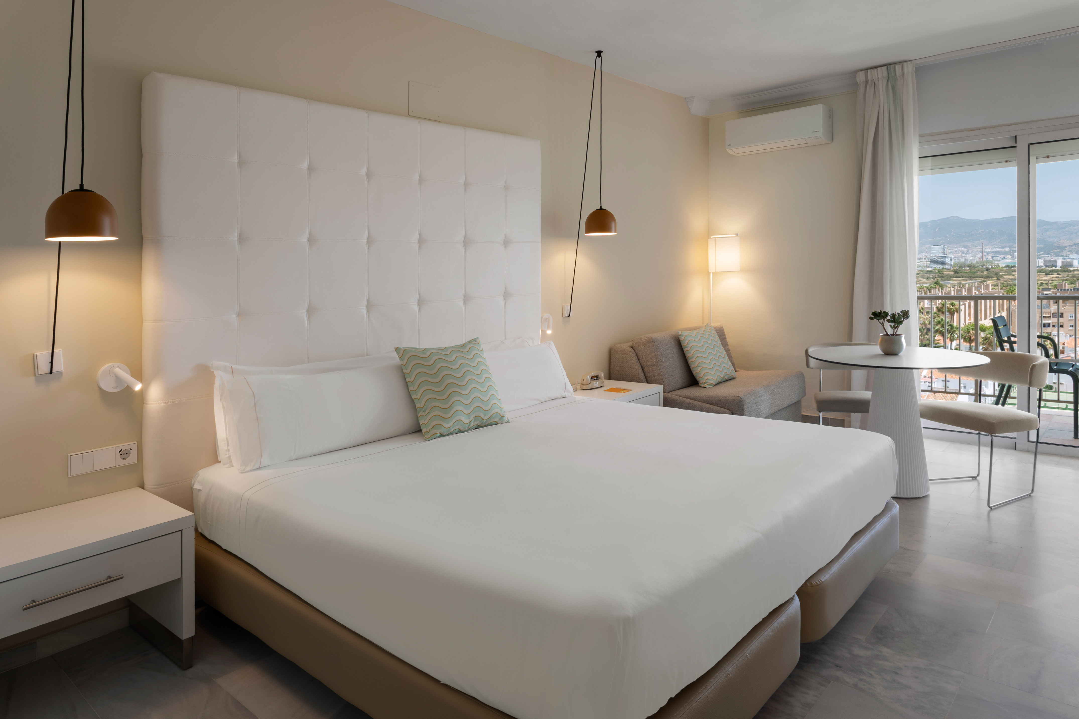 Suite de hotel moderna con cama doble, área de estar y balcón con vistas.