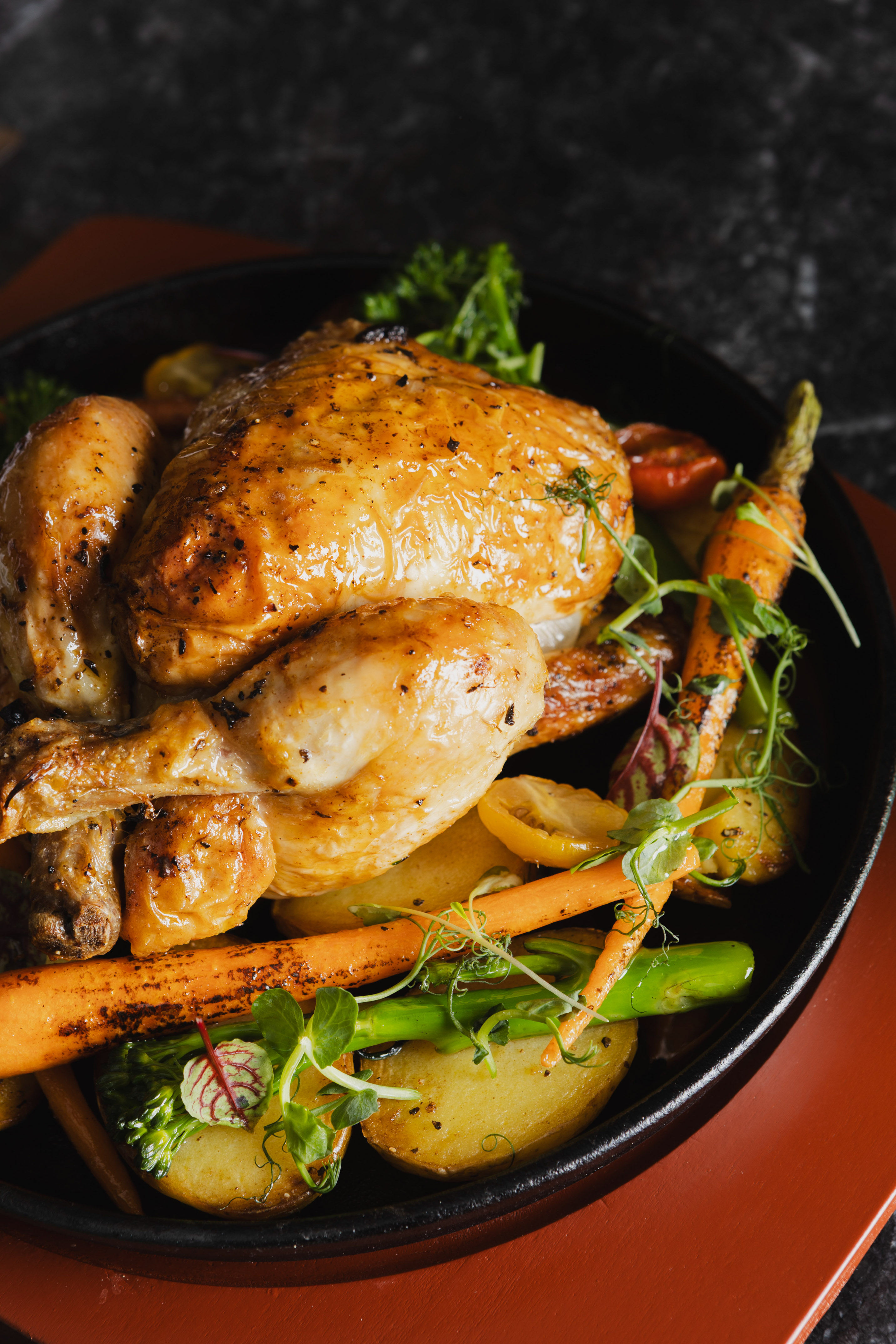 Golden roasted whole chicken and vegetables served in a black skillet.