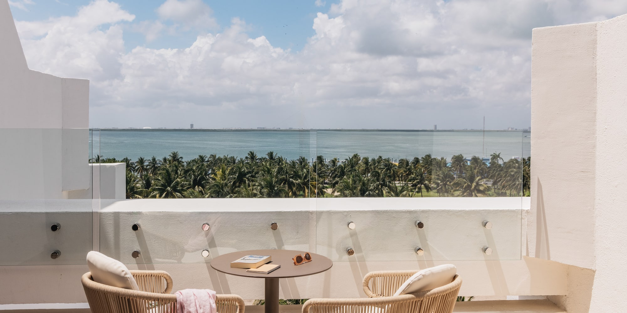 Balcony with ocean view, lush palm trees, outdoor chairs, and table.