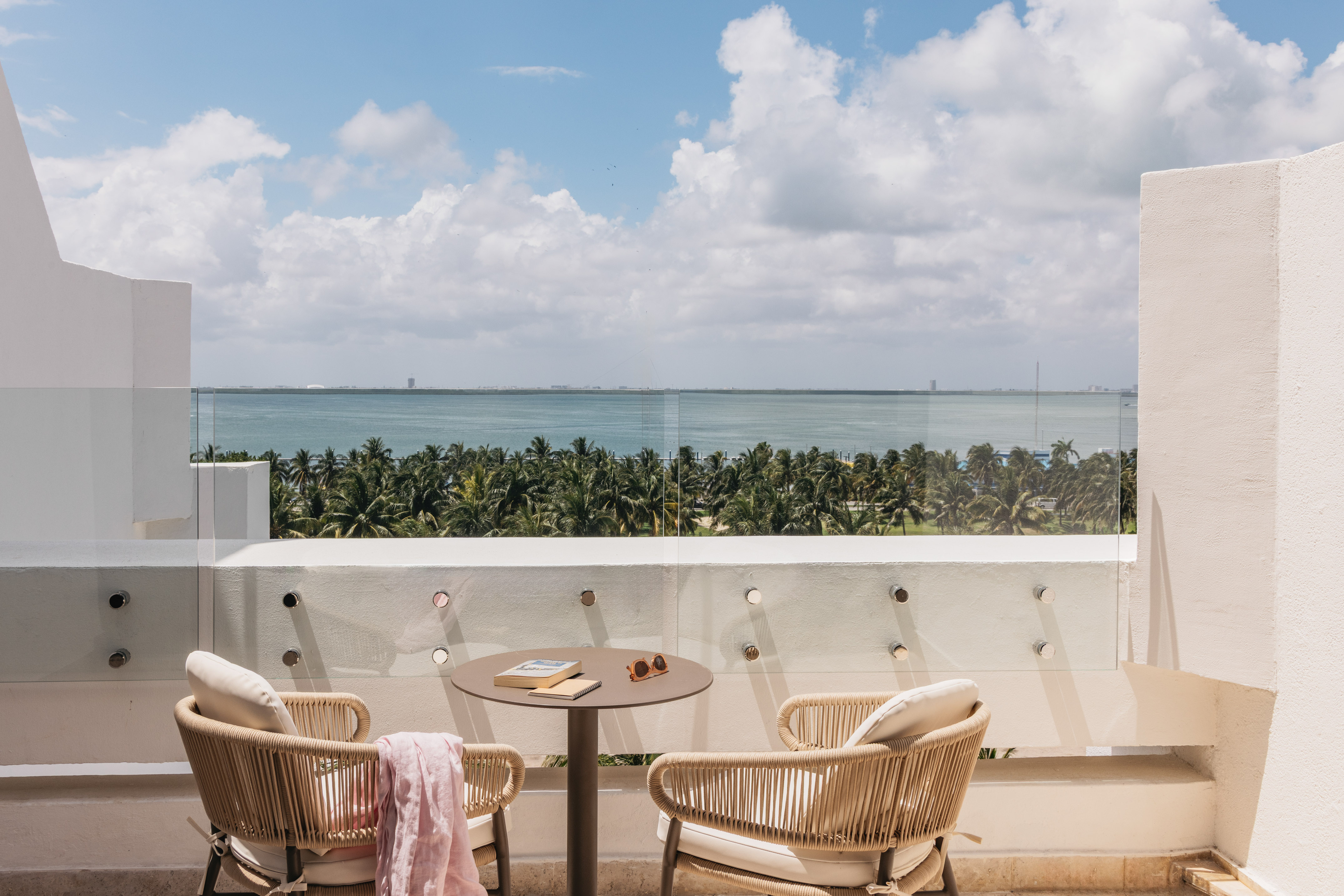Balcony with ocean view, lush palm trees, outdoor chairs, and table.