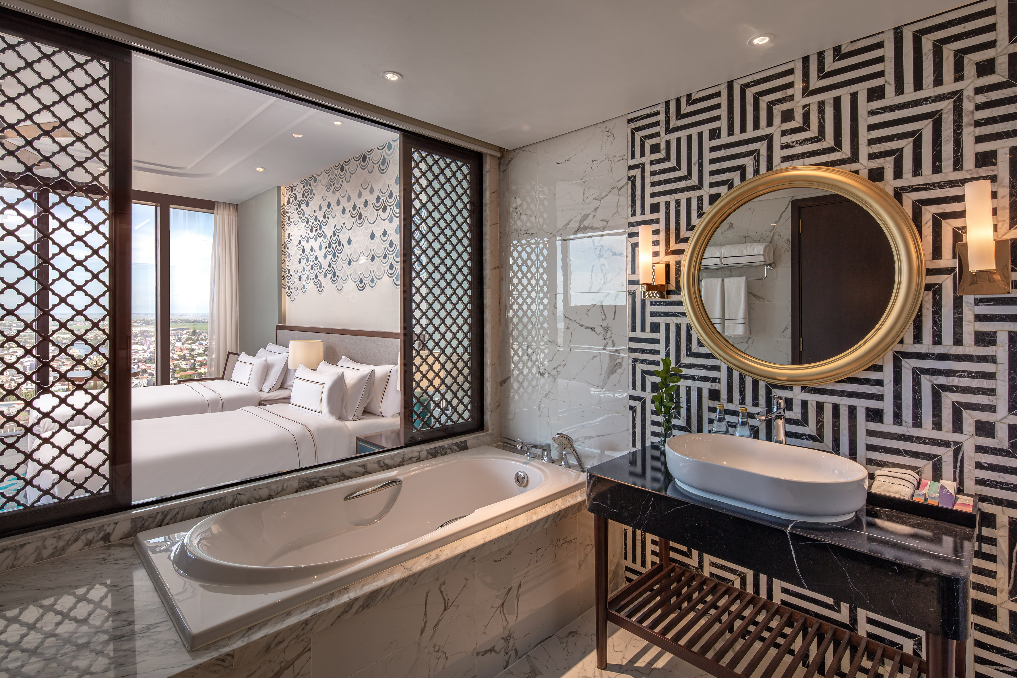Luxury hotel bathroom with bathtub, black geometric tiles, and view to modern bedroom.