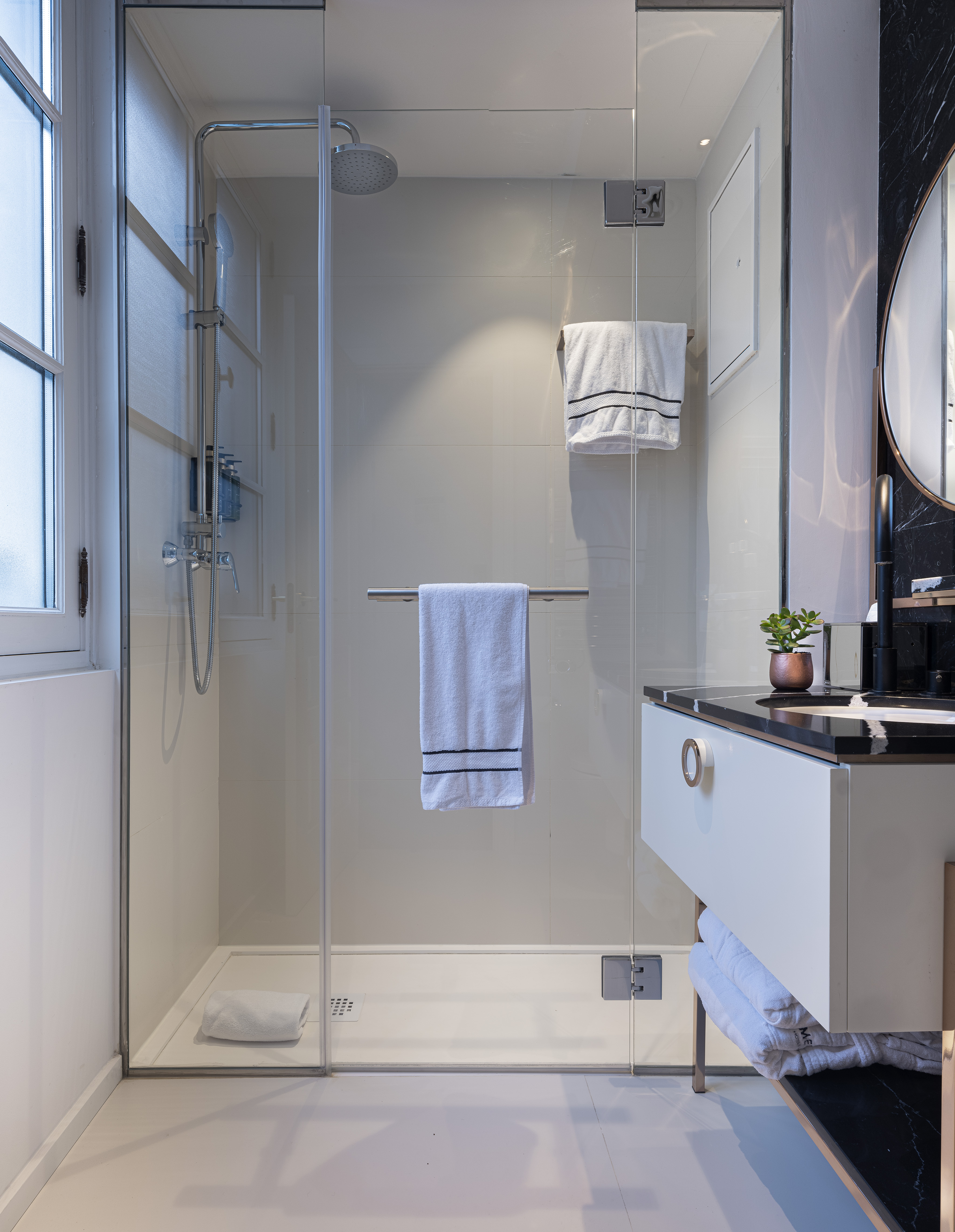 Modern bathroom with glass shower enclosure, black marble vanity, and white towels.