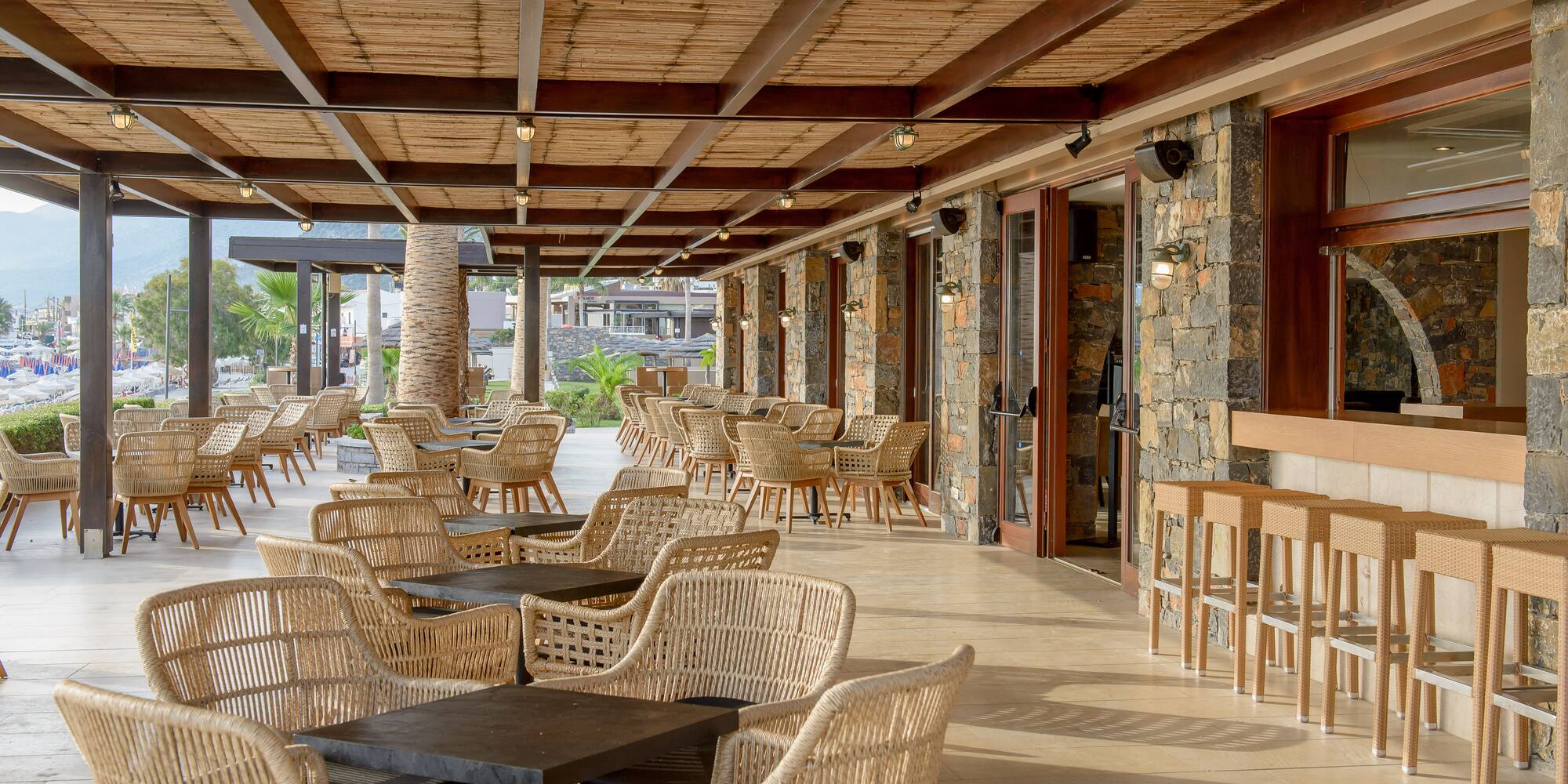 Spacious outdoor resort restaurant patio with rattan chairs, bamboo ceiling, and bar.