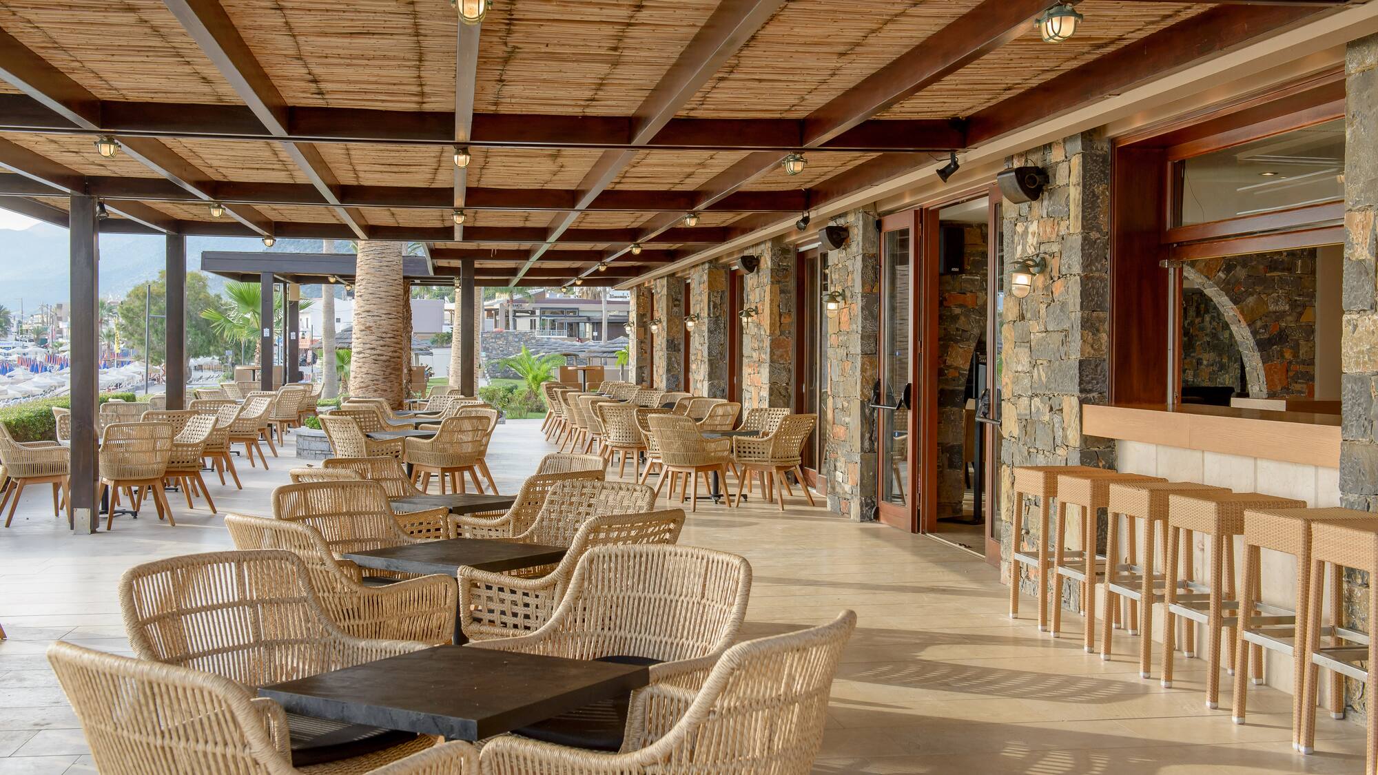 Spacious outdoor resort restaurant patio with rattan chairs, bamboo ceiling, and bar.