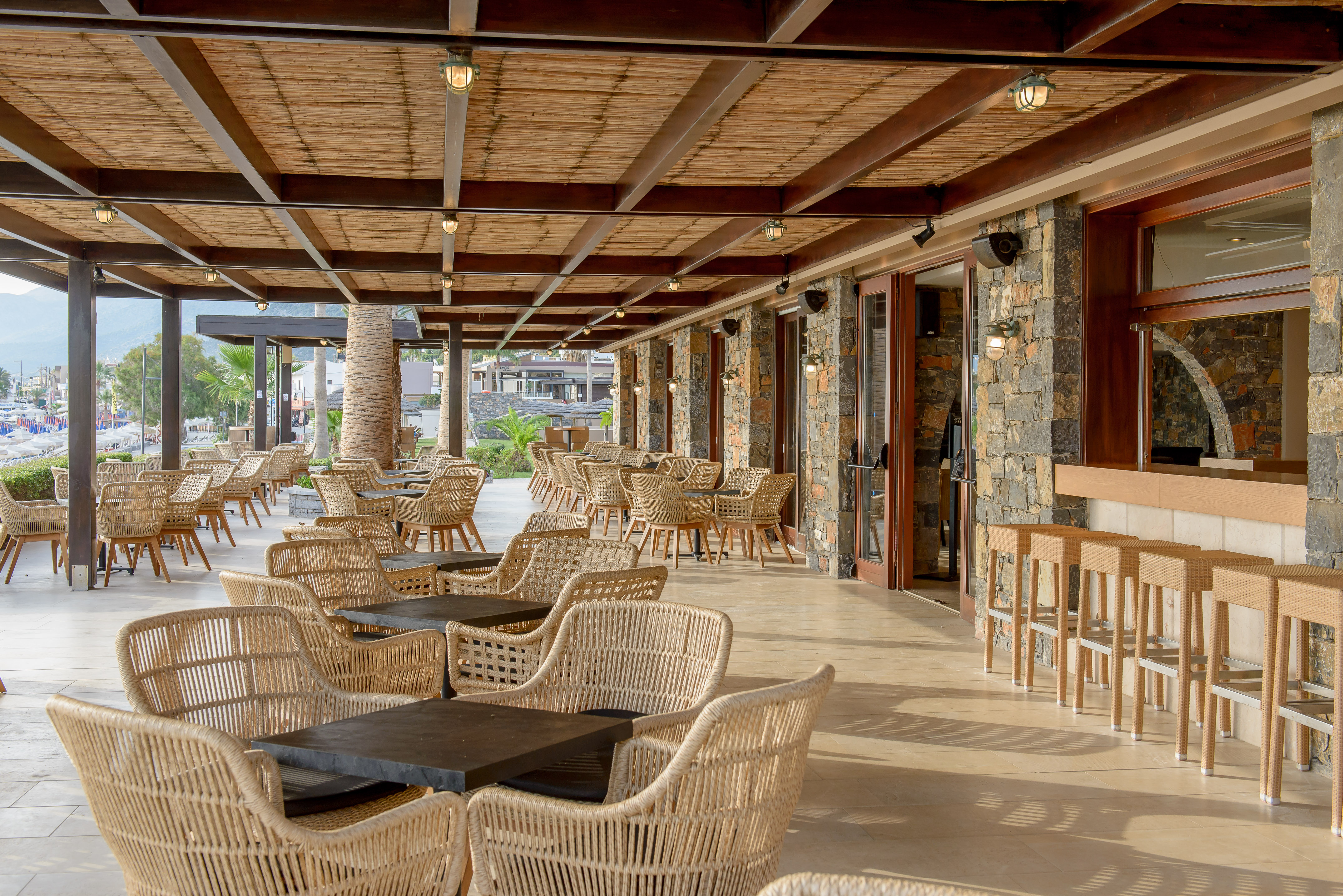 Spacious outdoor resort restaurant patio with rattan chairs, bamboo ceiling, and bar.