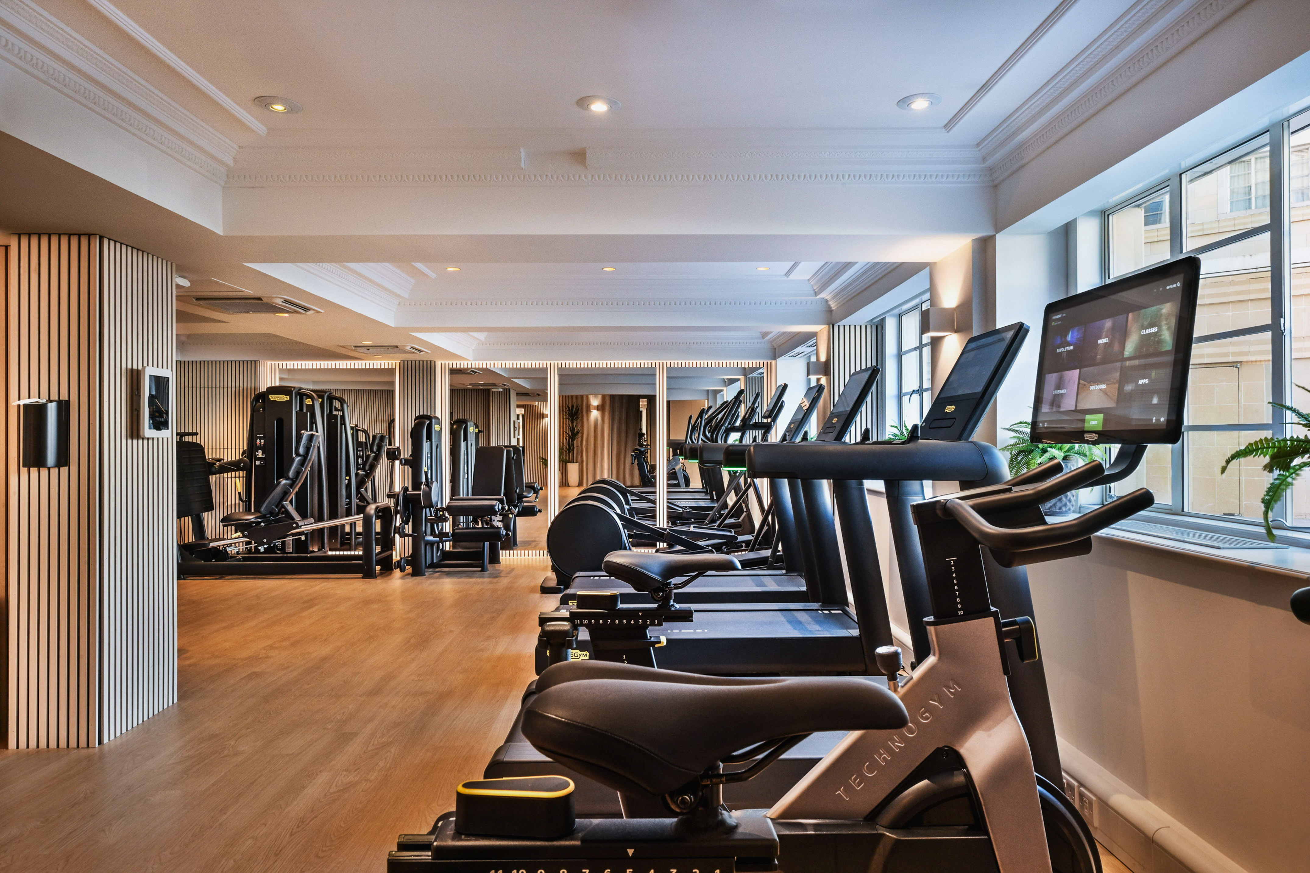 Modern gym interior with Technogym spin bikes, treadmills, and weight machines.