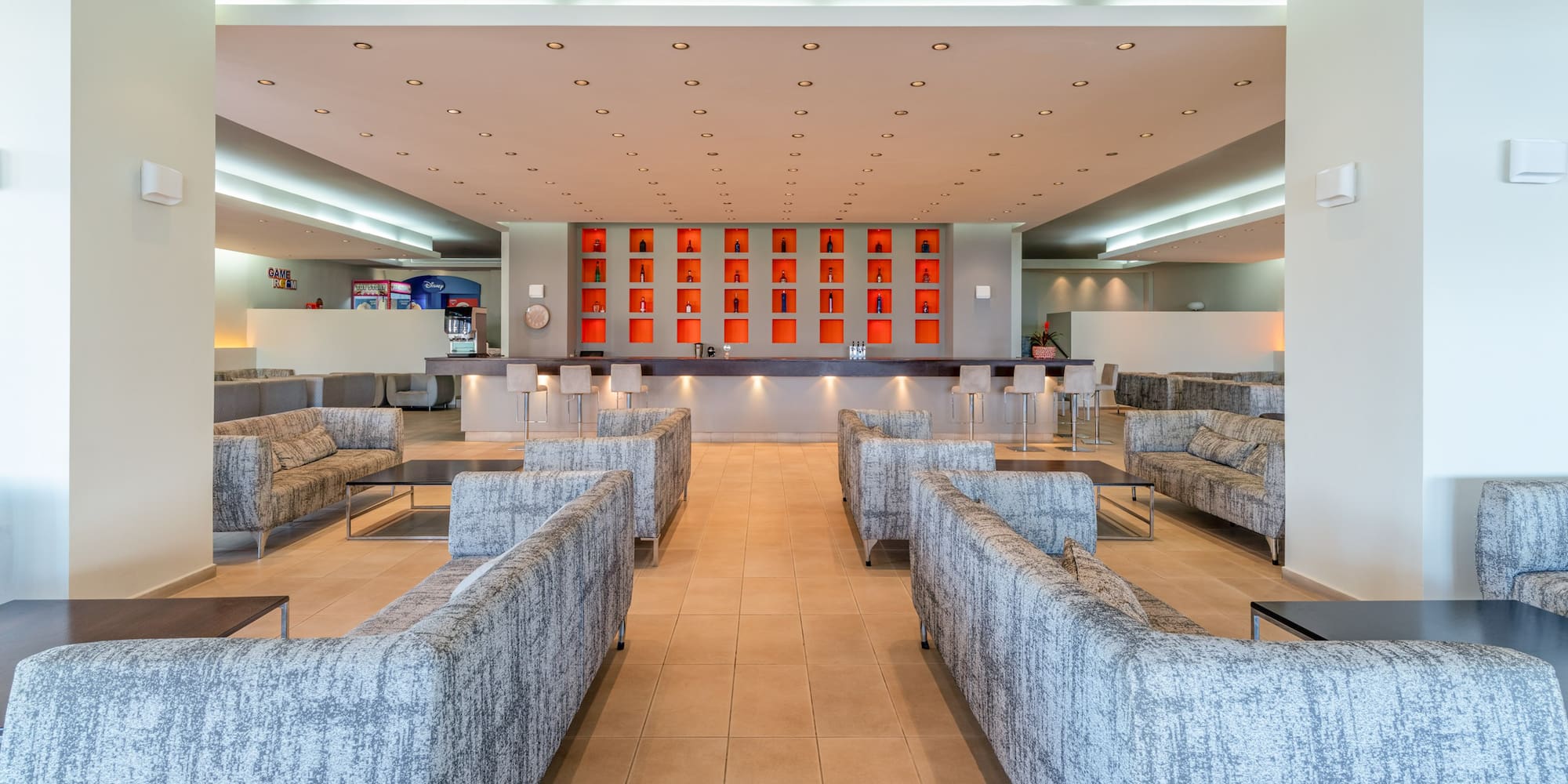 Modern hotel lounge bar with grey sofas and orange bottle display.