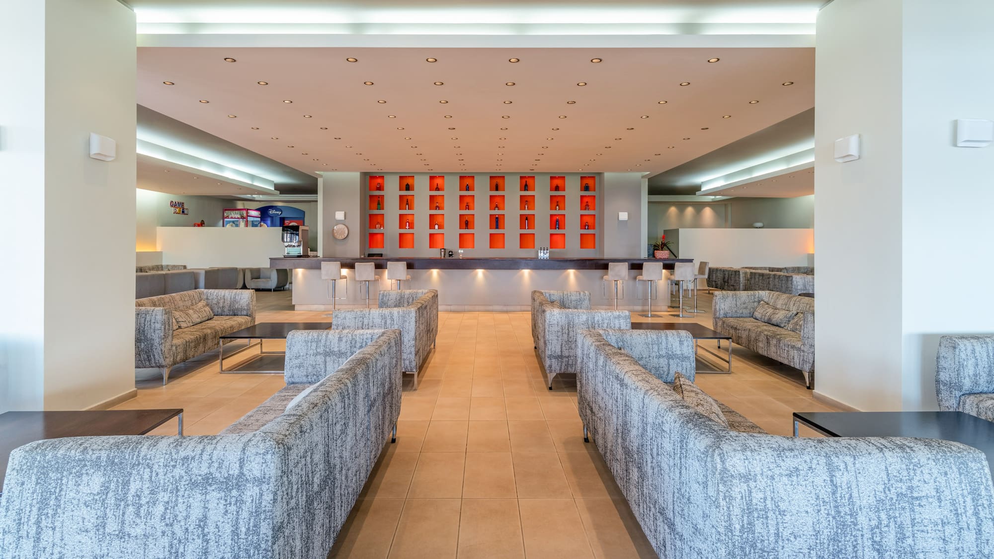 Modern hotel lounge bar with grey sofas and orange bottle display.