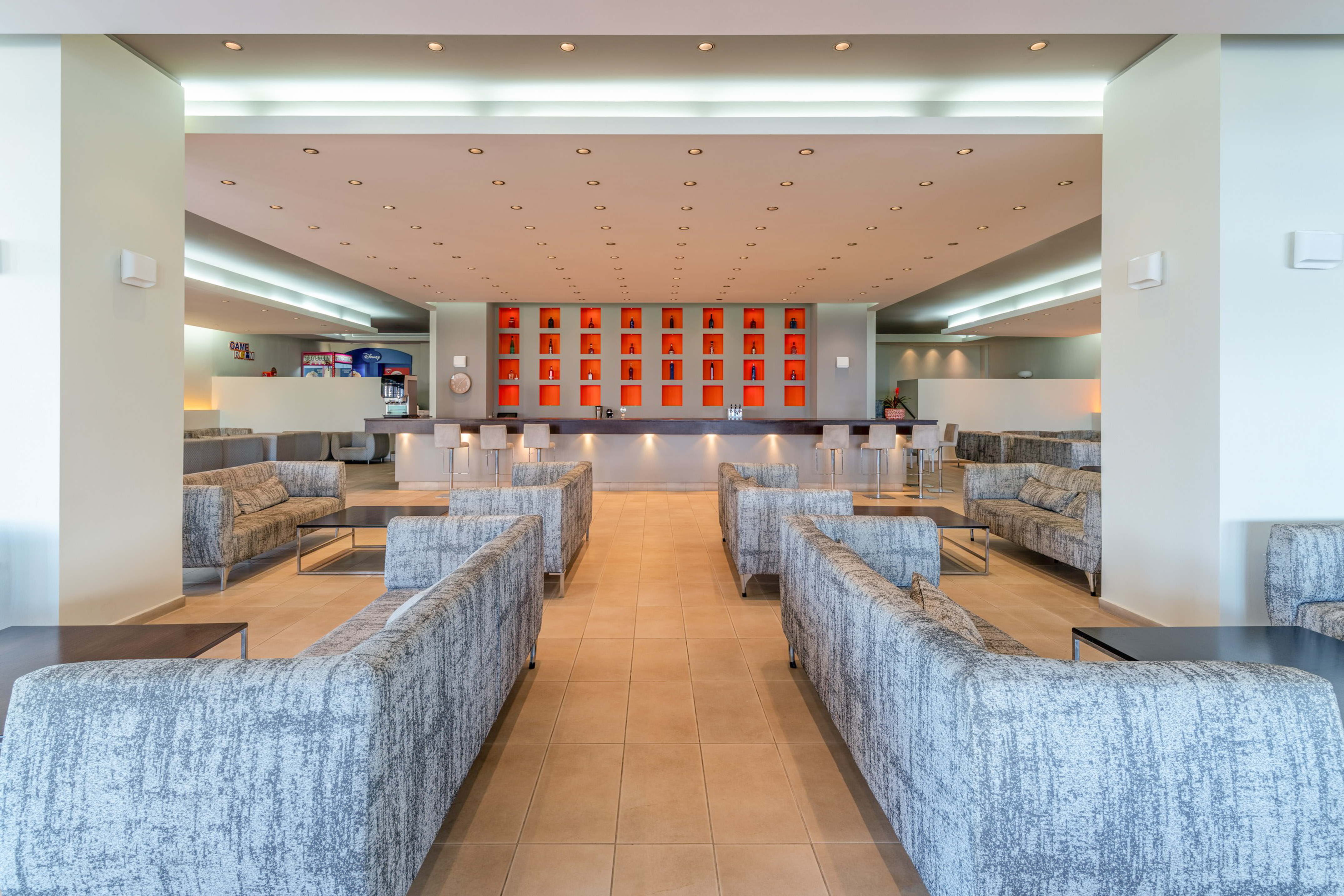 Modern hotel lounge bar with grey sofas and orange bottle display.