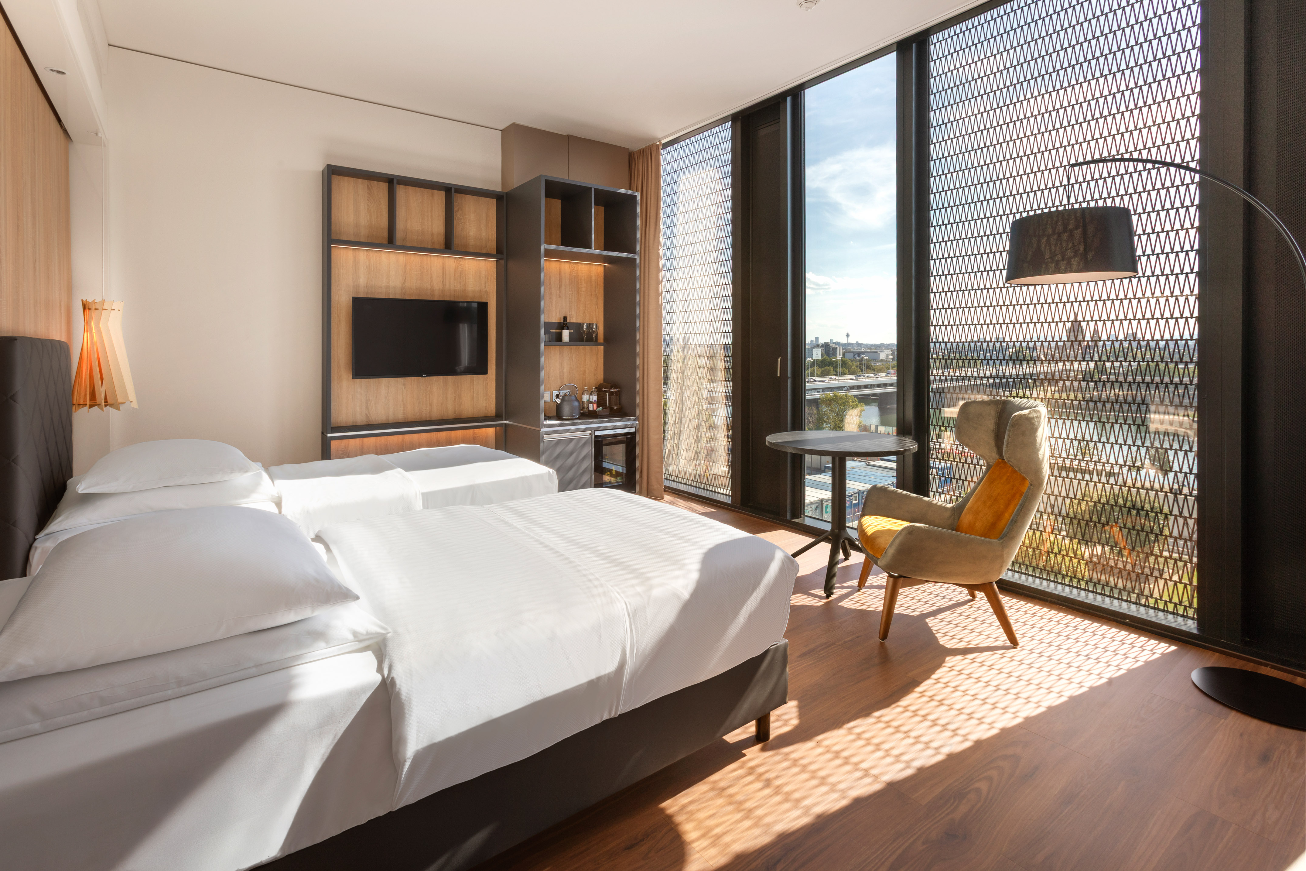 Modern hotel room with twin beds, city view, and large windows.