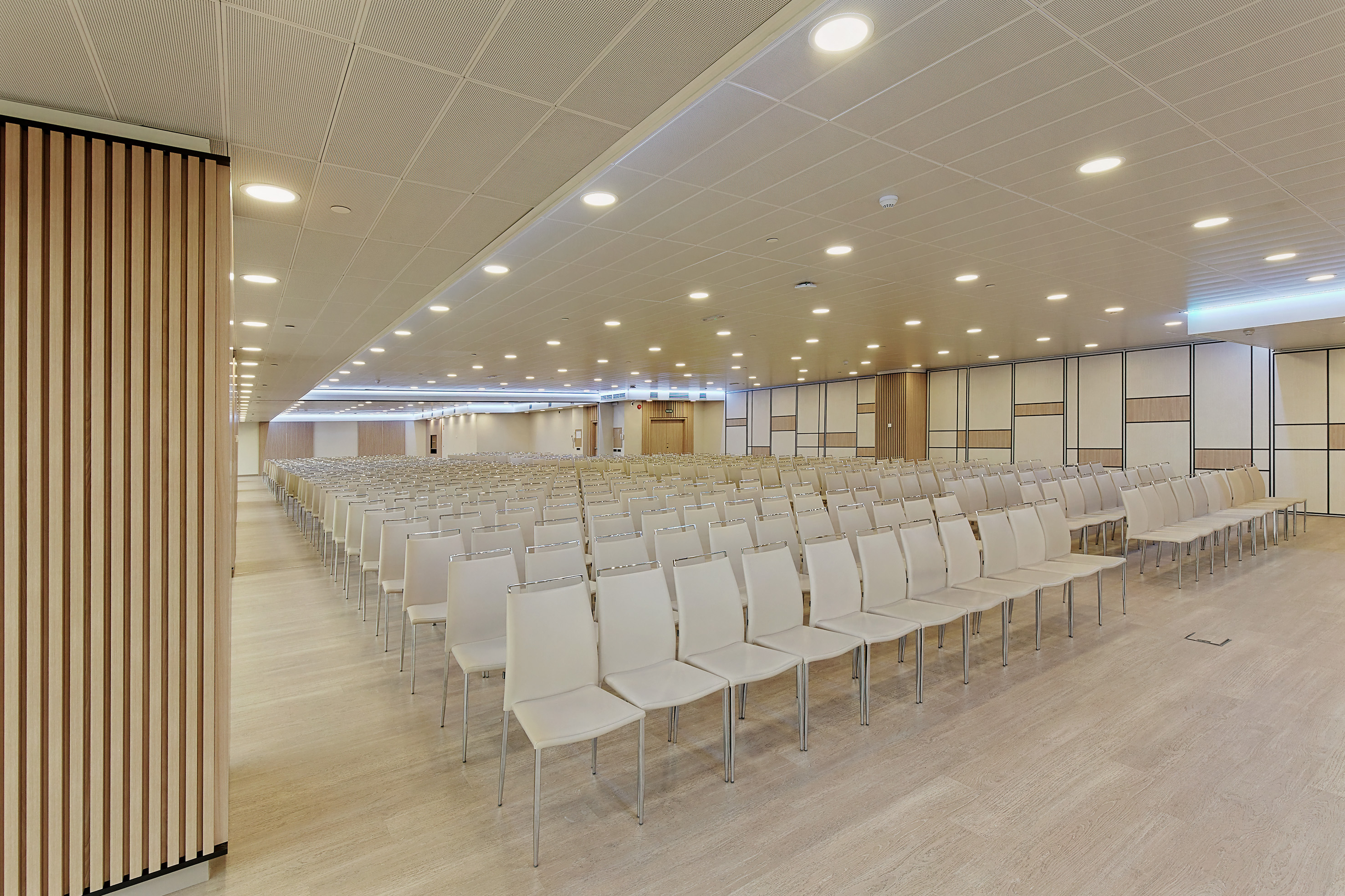 Modern empty conference room with rows of beige chairs and wood paneling.