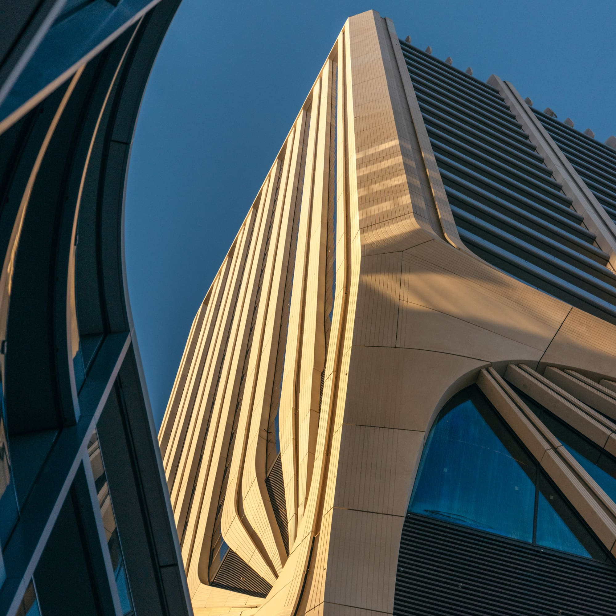 Modern skyscraper with undulating beige facade under clear blue sky.